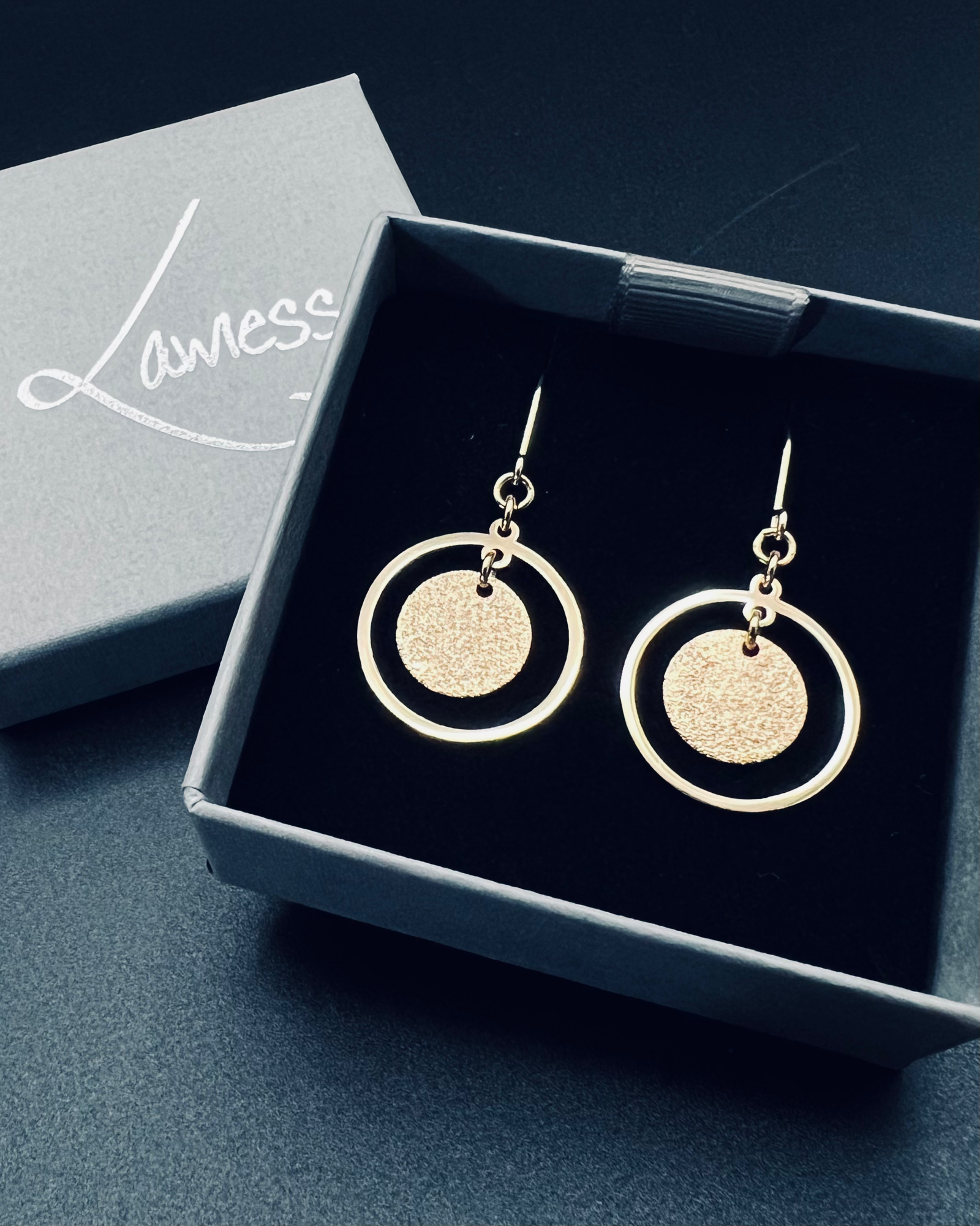 Gold stainless steel halo earrings featuring a circular frame with a textured gold disc suspended inside, lightweight 4 cm design — Lawless Jewellery.