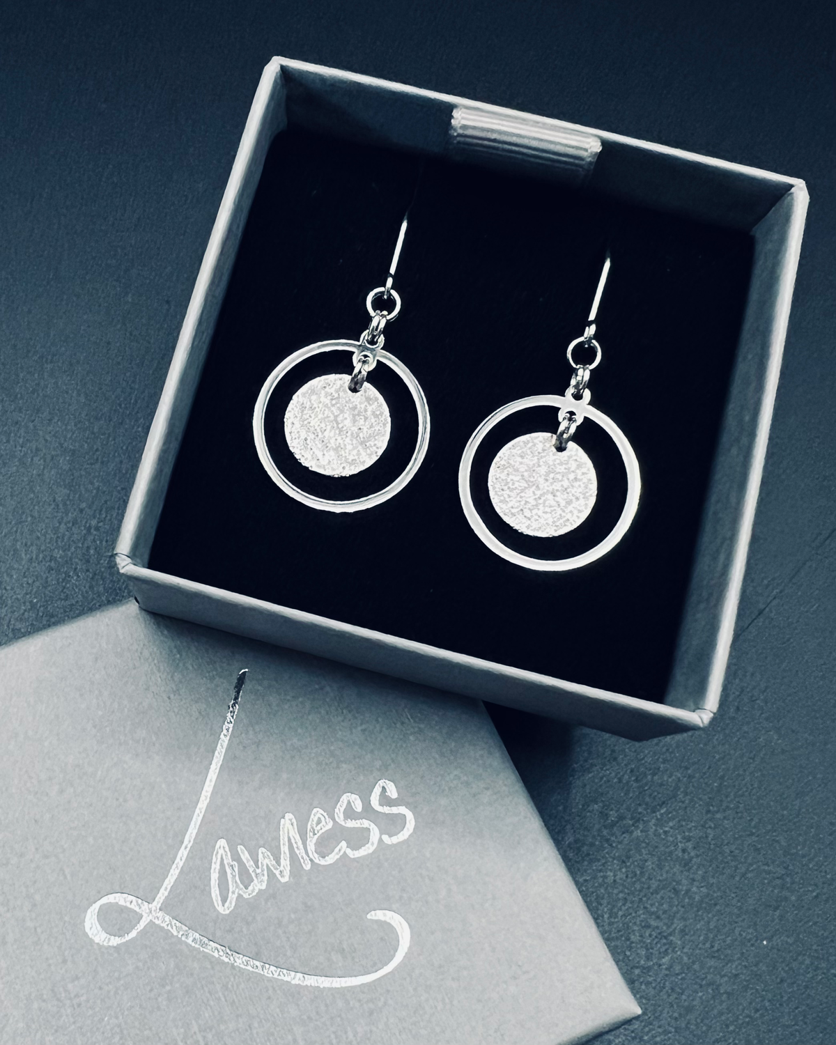 Silver stainless steel halo earrings with a circular frame and suspended textured disc, minimalist 4 cm design — Lawless Jewellery.