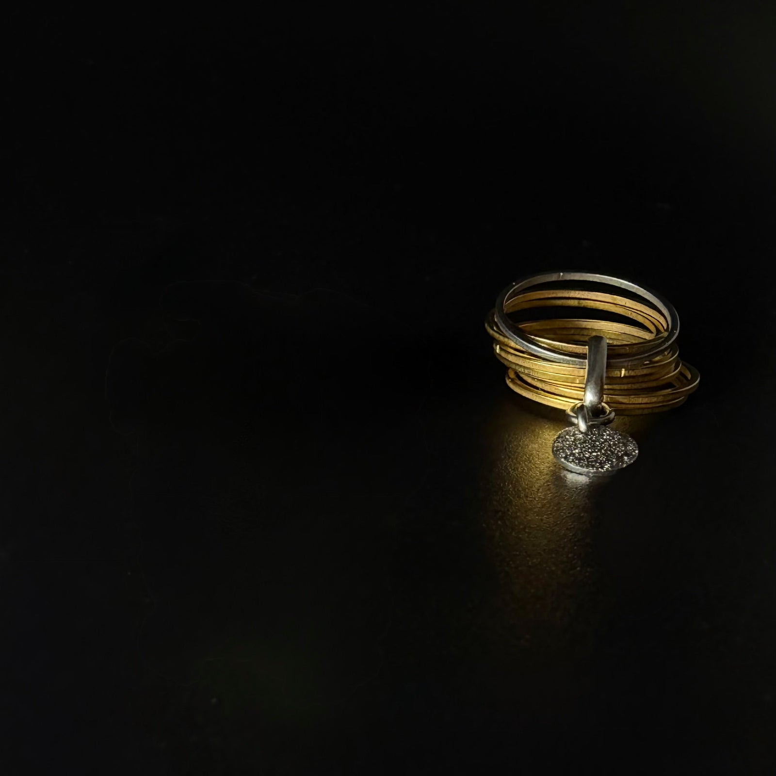 Gold stainless steel fidget ring featuring seven silver bands, one rotating silver band, and a suspended textured gold disc — Lawless Jewellery.
