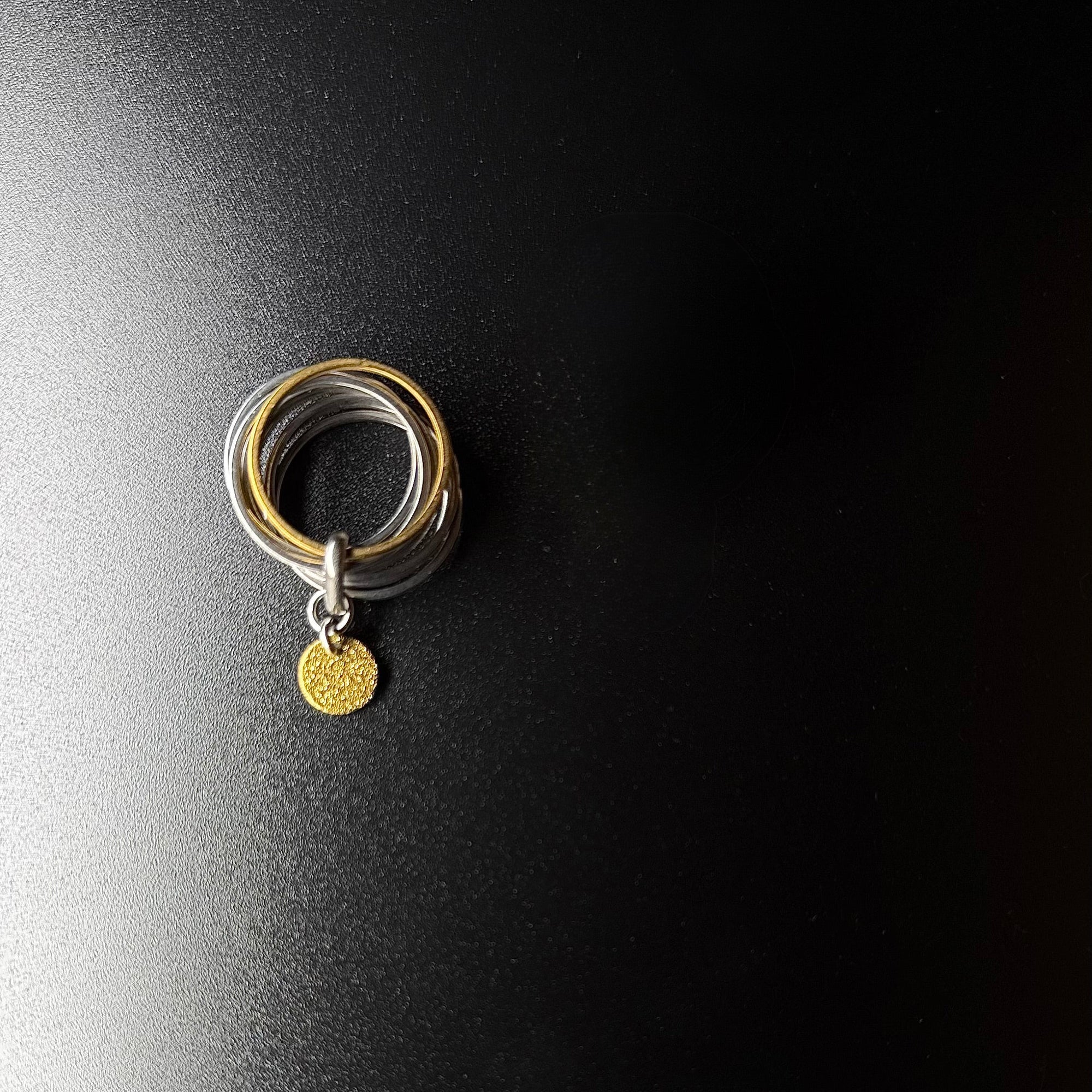 Silver stainless steel fidget ring featuring seven silver bands, one rotating gold band, and a suspended textured gold disc — Lawless Jewellery.