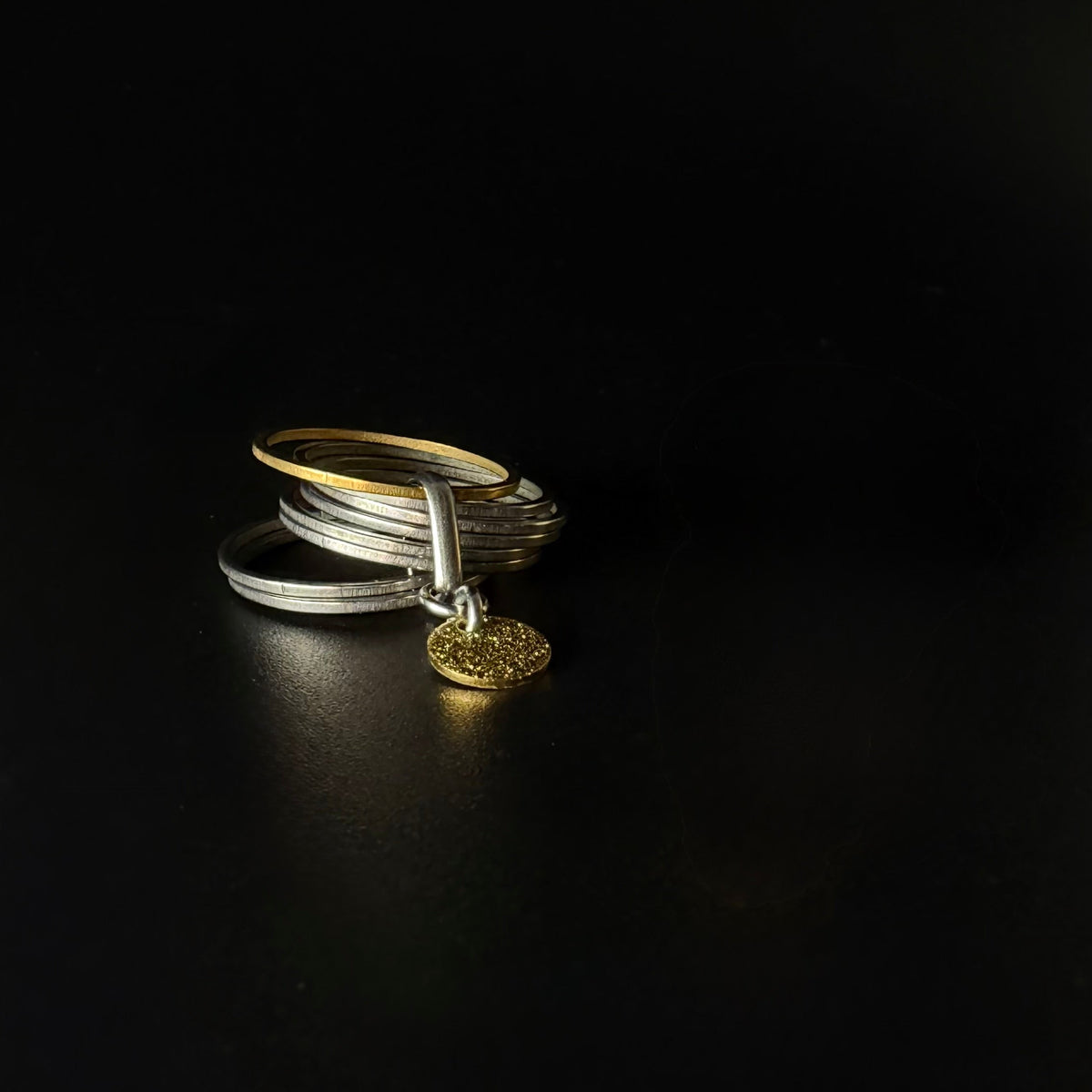 Silver stainless steel fidget ring featuring seven silver bands, one rotating gold band, and a suspended textured gold disc — Lawless Jewellery.