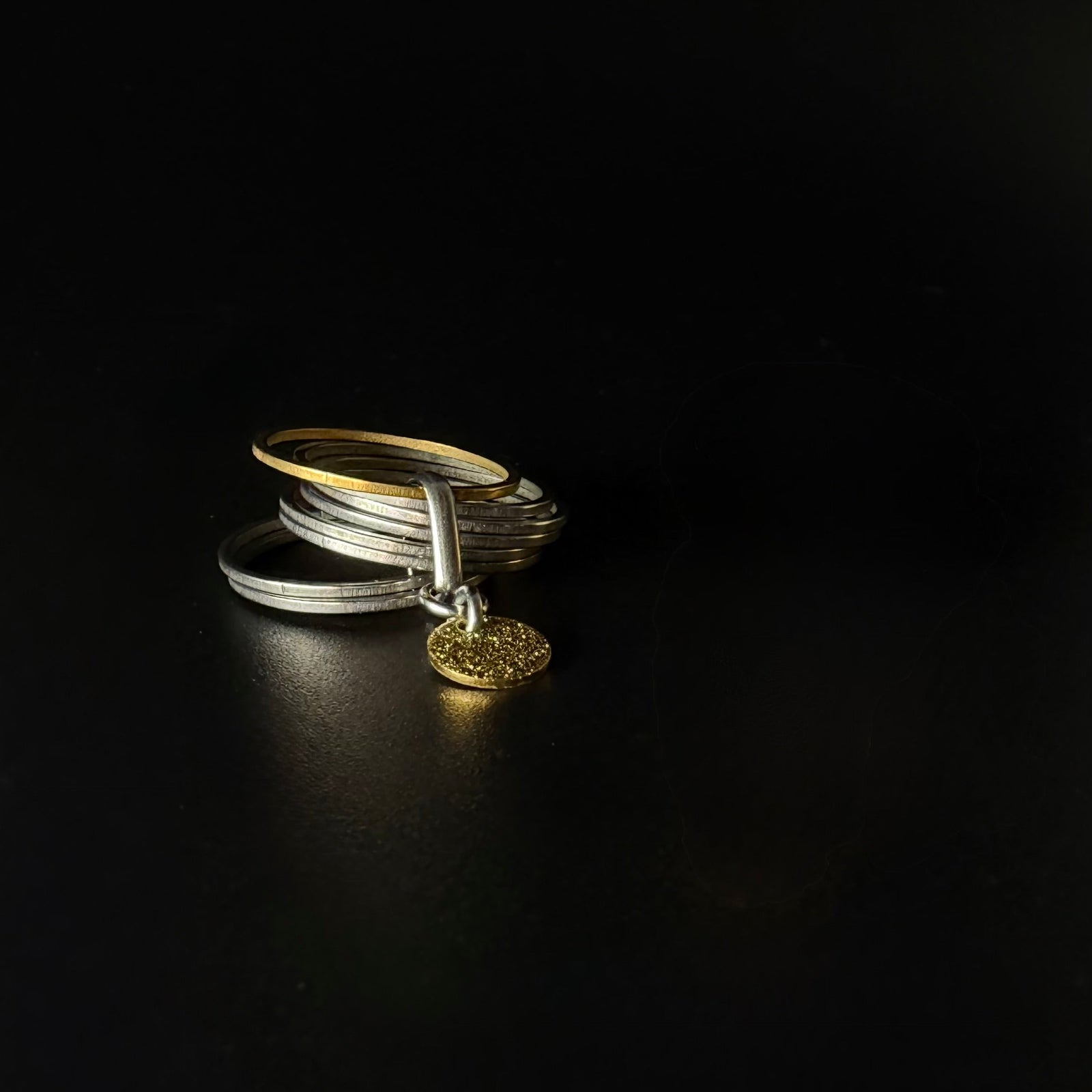 Silver stainless steel fidget ring featuring seven silver bands, one rotating gold band, and a suspended textured gold disc — Lawless Jewellery.