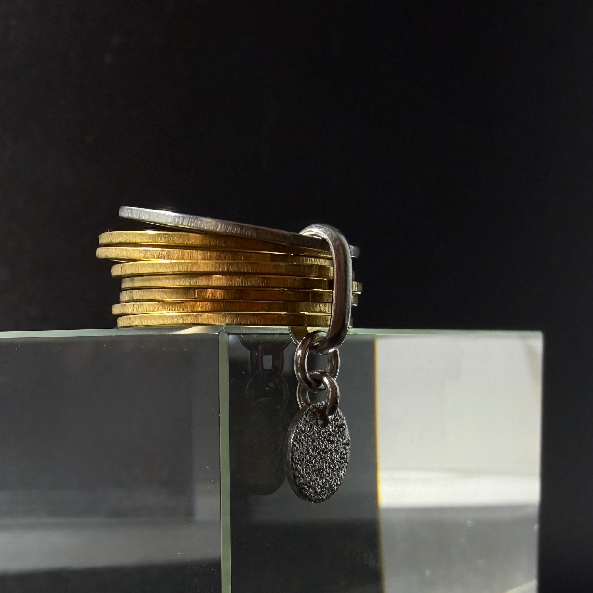 Gold stainless steel fidget ring featuring seven silver bands, one rotating silver band, and a suspended textured gold disc — Lawless Jewellery.