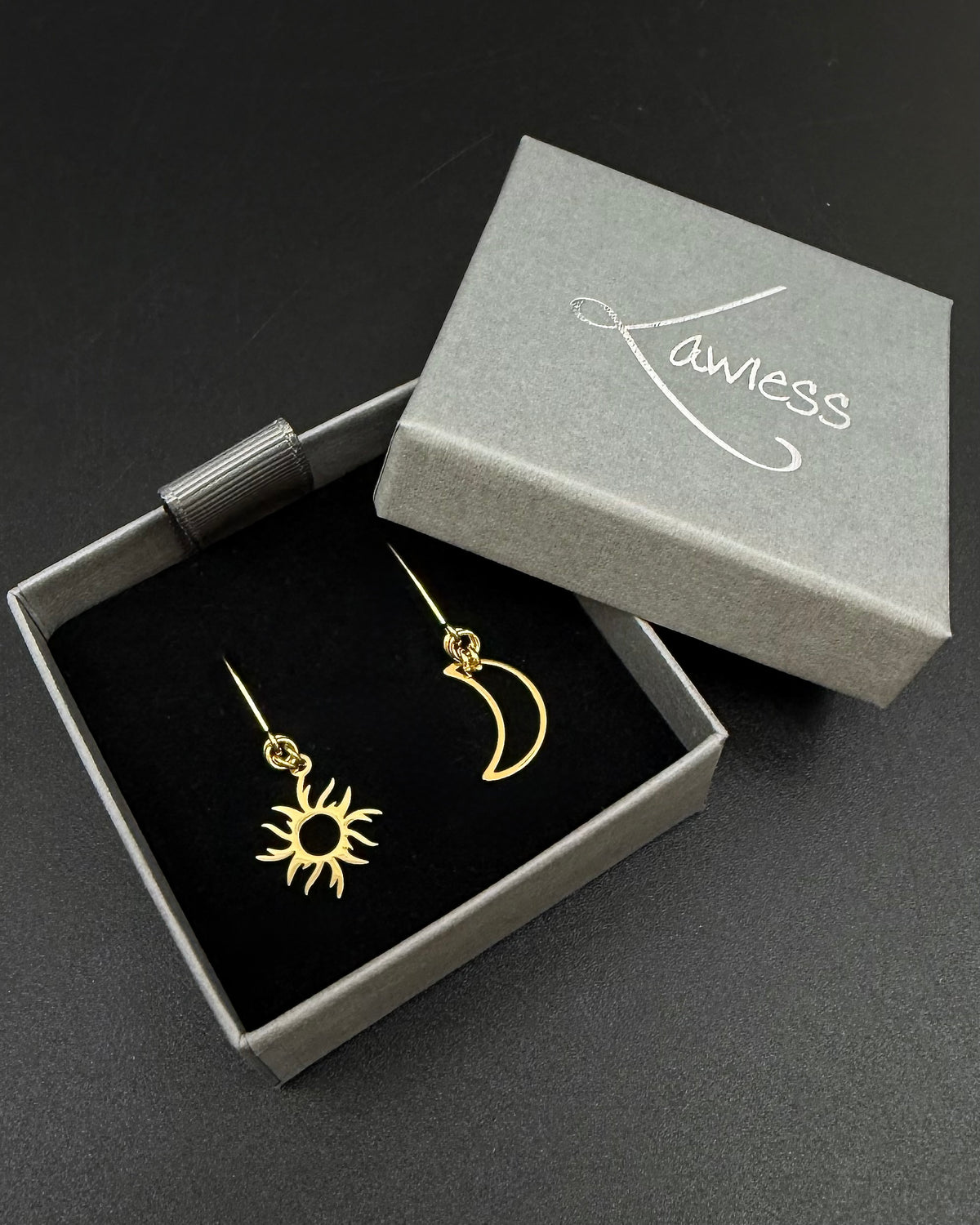 Gold sun and moon mismatched earrings in polished stainless steel, Eos Dawn Earrings by Lawless Jewellery on a dark background.