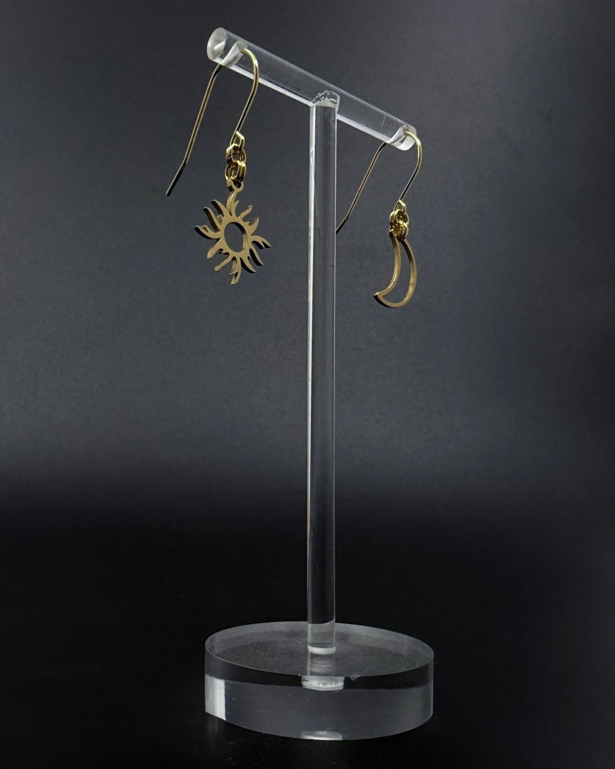 Gold sun and moon mismatched earrings in polished stainless steel, Eos Dawn Earrings by Lawless Jewellery on a dark background.