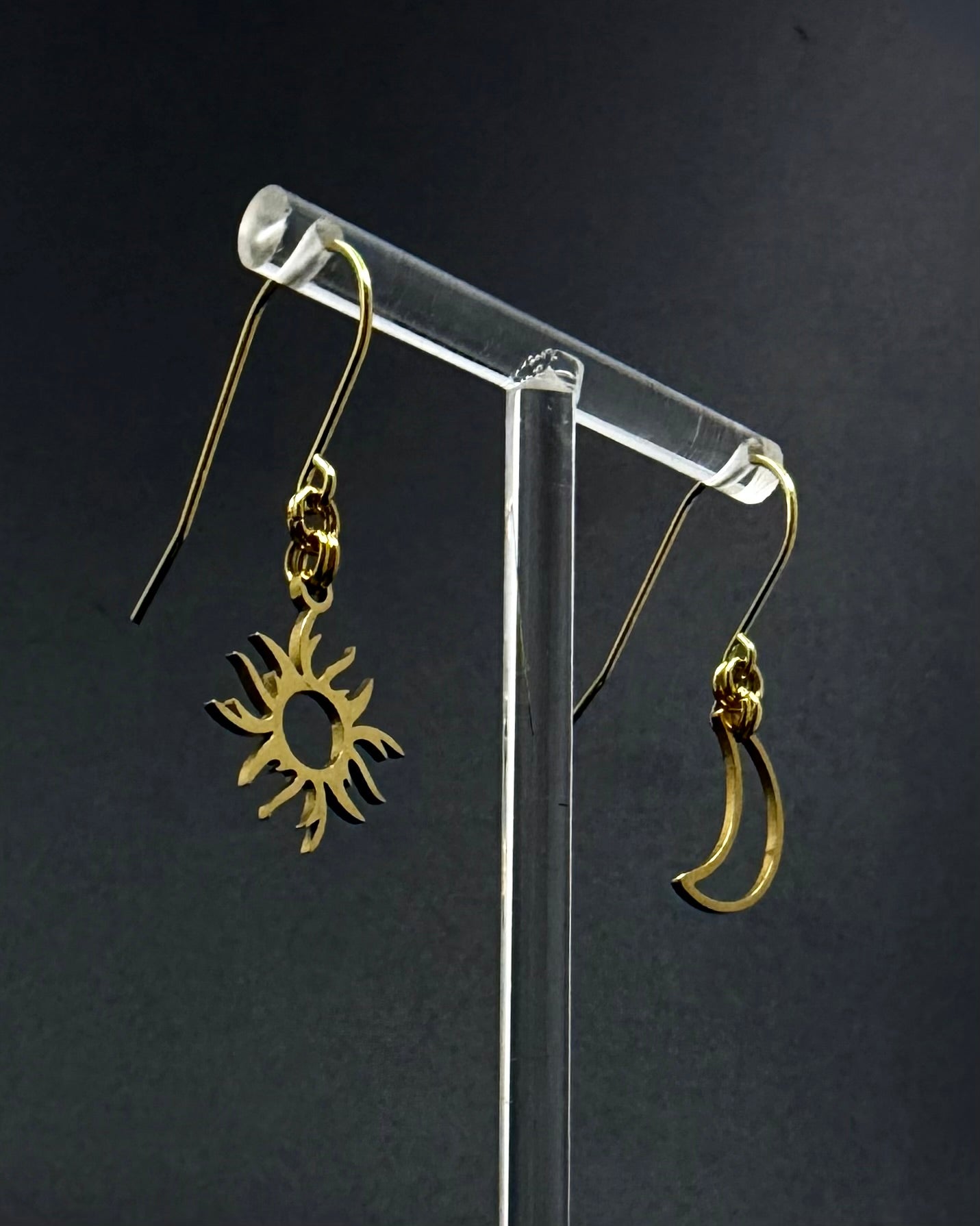 Gold sun and moon mismatched earrings in polished stainless steel, Eos Dawn Earrings by Lawless Jewellery on a dark background.