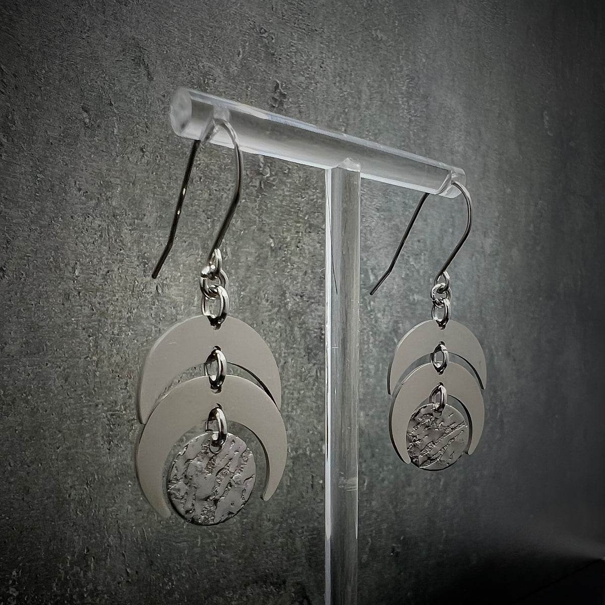 All-silver stainless steel lunar earrings featuring layered crescent shapes with a textured disc, 20 mm wide with a 4 cm drop — Lawless Jewellery.