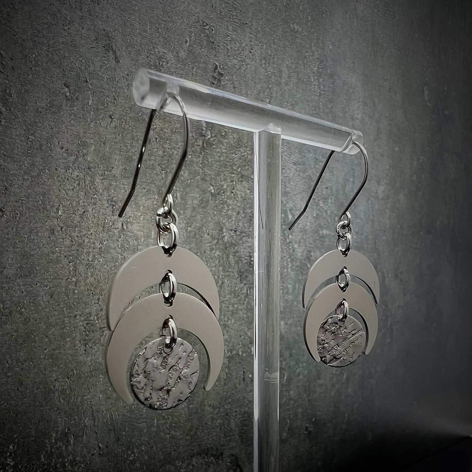 All-silver stainless steel lunar earrings featuring layered crescent shapes with a textured disc, 20 mm wide with a 4 cm drop — Lawless Jewellery.