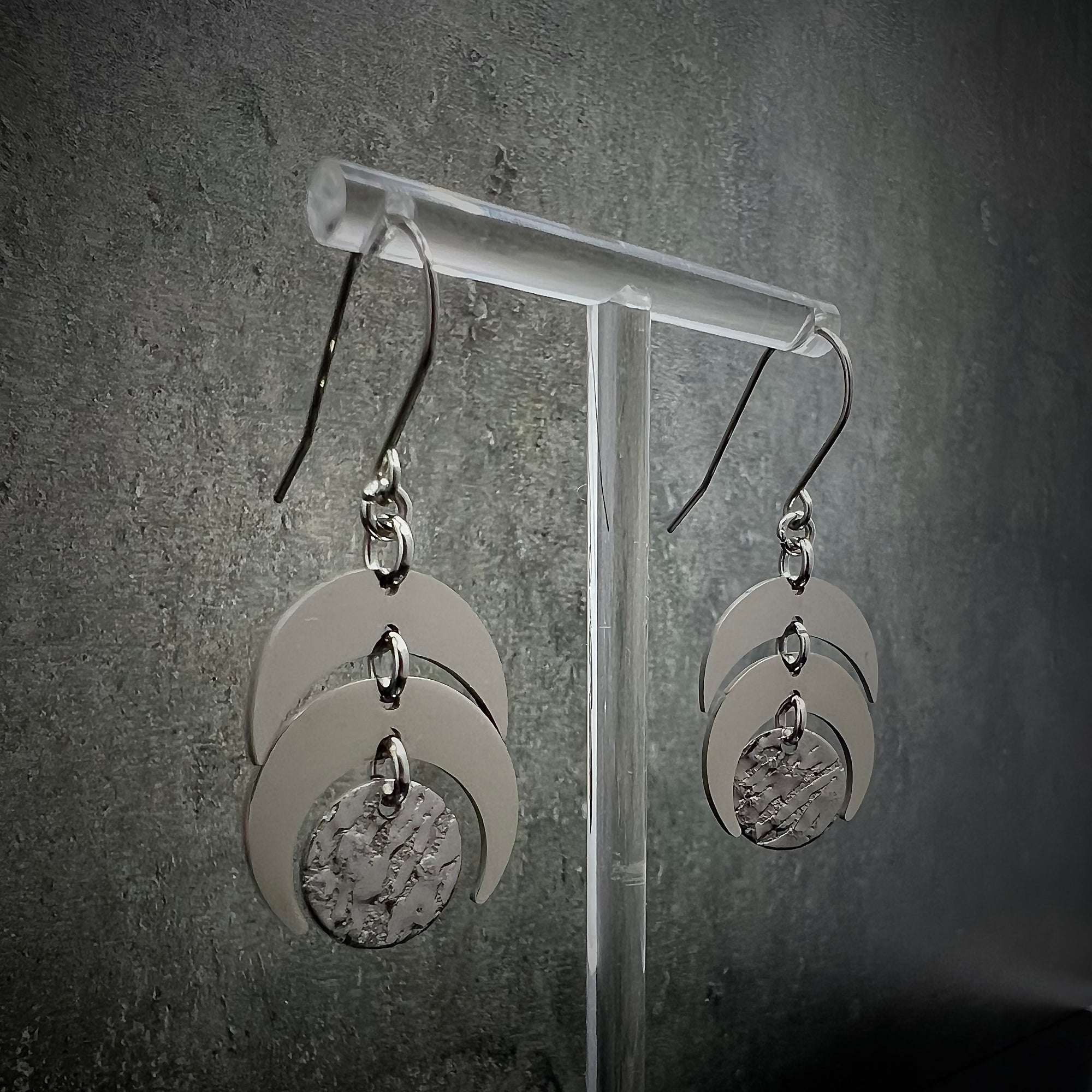 All-silver stainless steel lunar earrings featuring layered crescent shapes with a textured disc, 20 mm wide with a 4 cm drop — Lawless Jewellery.