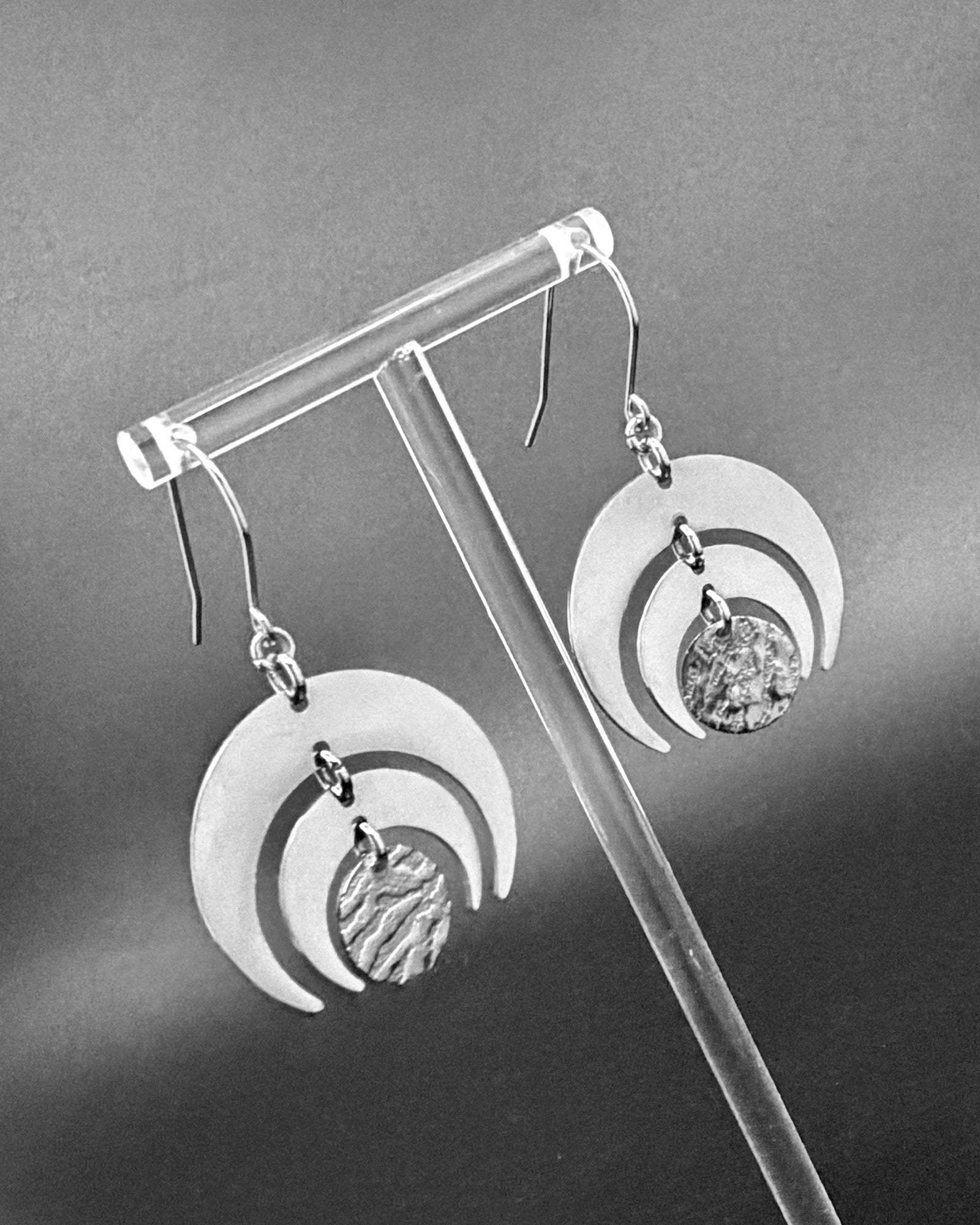 All silver stainless steel Luna Phase Earrings with triple crescent design and textured central disc, 30mm width. Lawless Jewellery made in Ireland