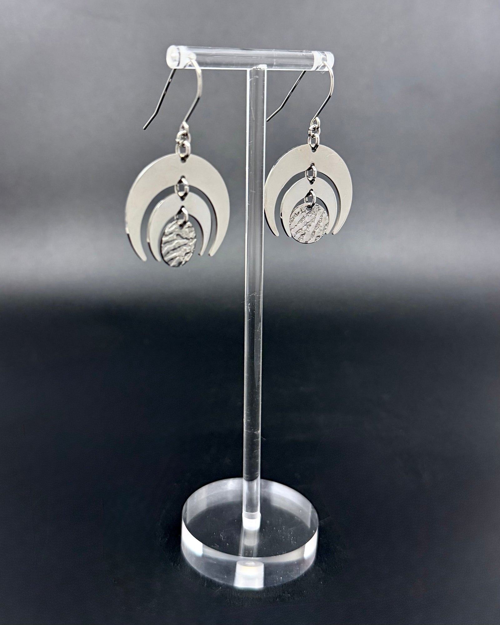 All silver stainless steel Luna Phase Earrings with triple crescent design and textured central disc, 30mm width. Lawless Jewellery made in Ireland