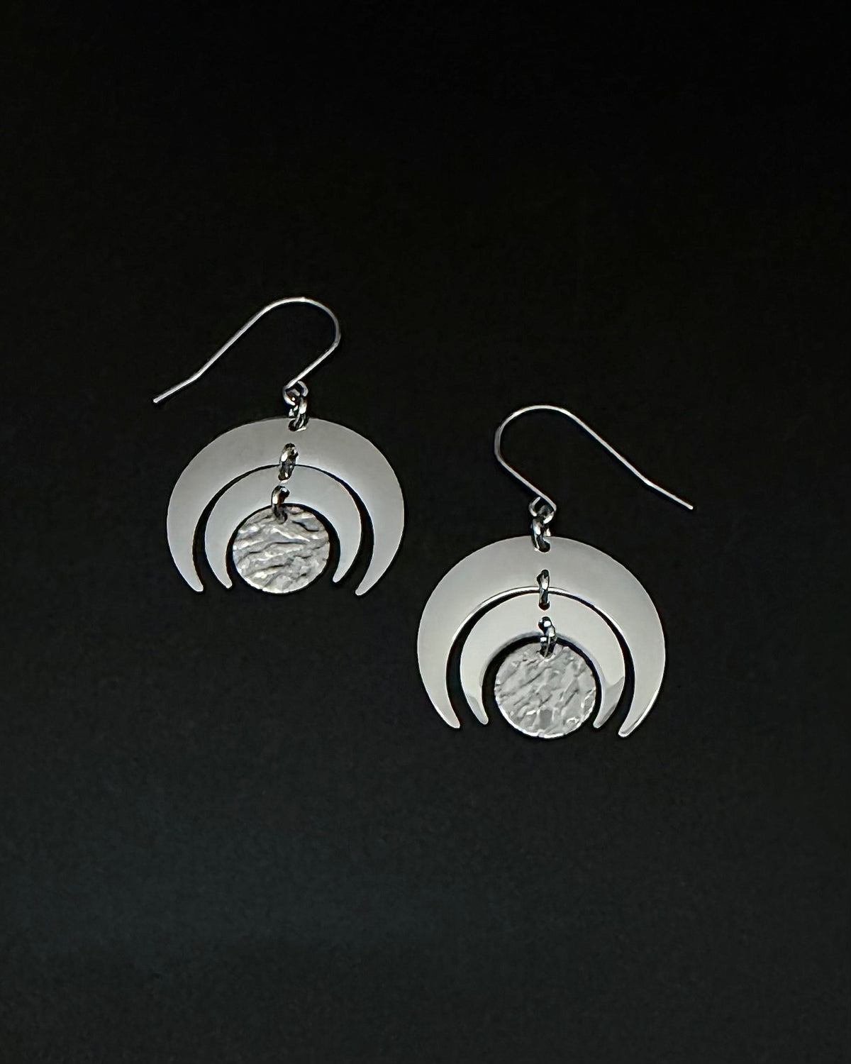 All silver stainless steel Luna Phase Earrings with triple crescent design and textured central disc, 30mm width. Lawless Jewellery made in Ireland