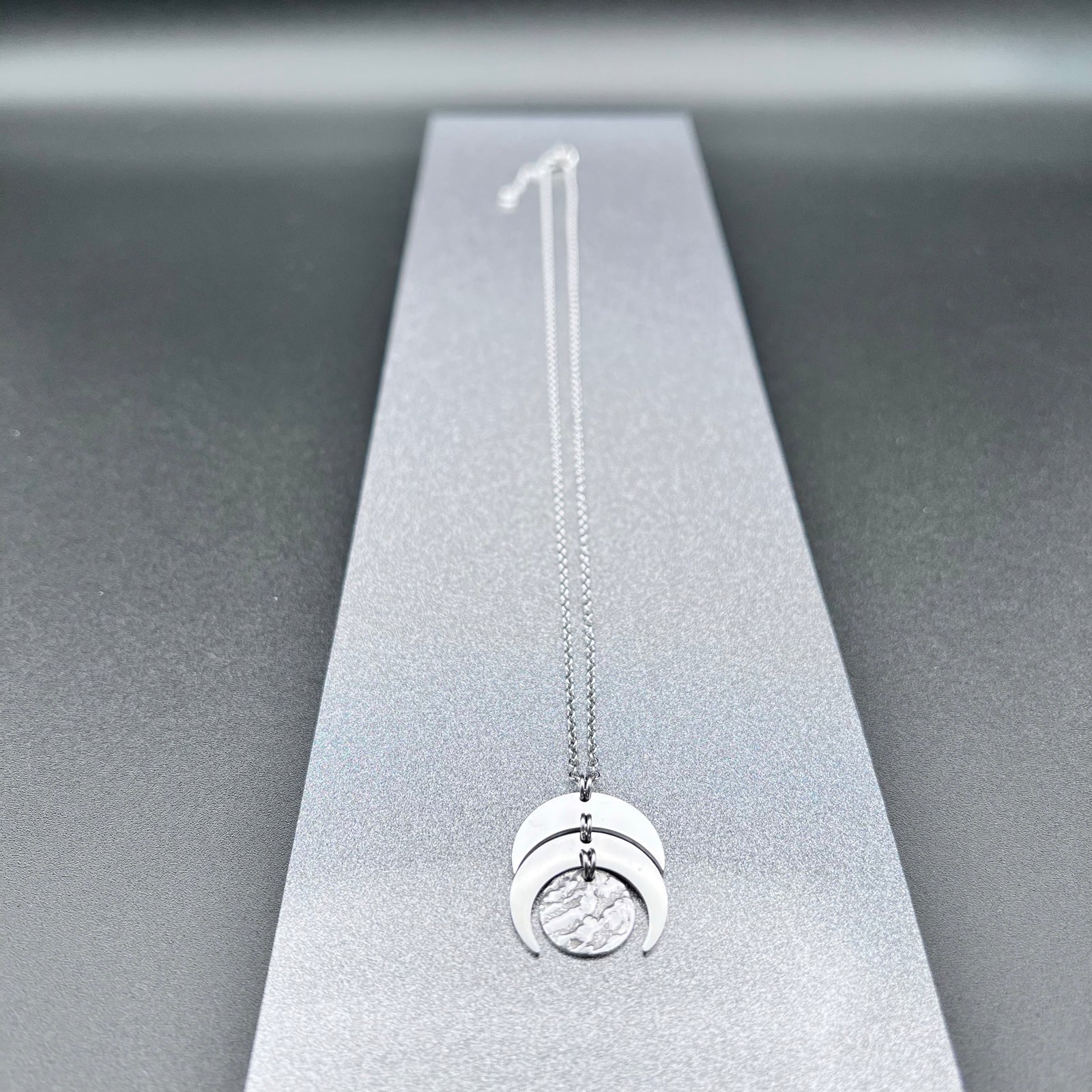 Silver stainless steel Luna Phase necklace with sculptural crescent and disc pendant on an adjustable chain, 20 mm wide — Lawless Jewellery.