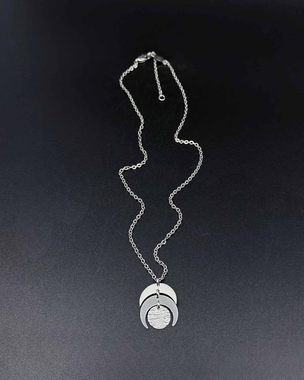 Silver Luna Phase necklace with sculptural crescent moon pendant and textured lunar disc on stainless steel chain, minimalist celestial design