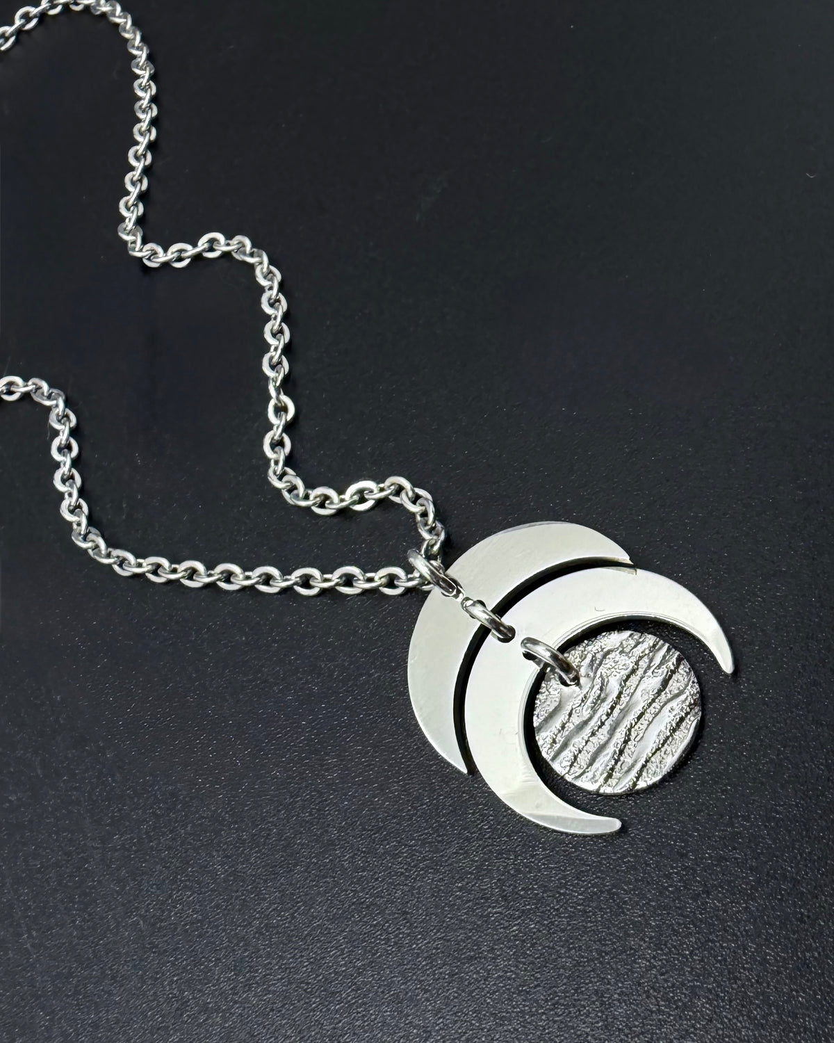 Silver Luna Phase necklace with sculptural crescent moon pendant and textured lunar disc on stainless steel chain, minimalist celestial design