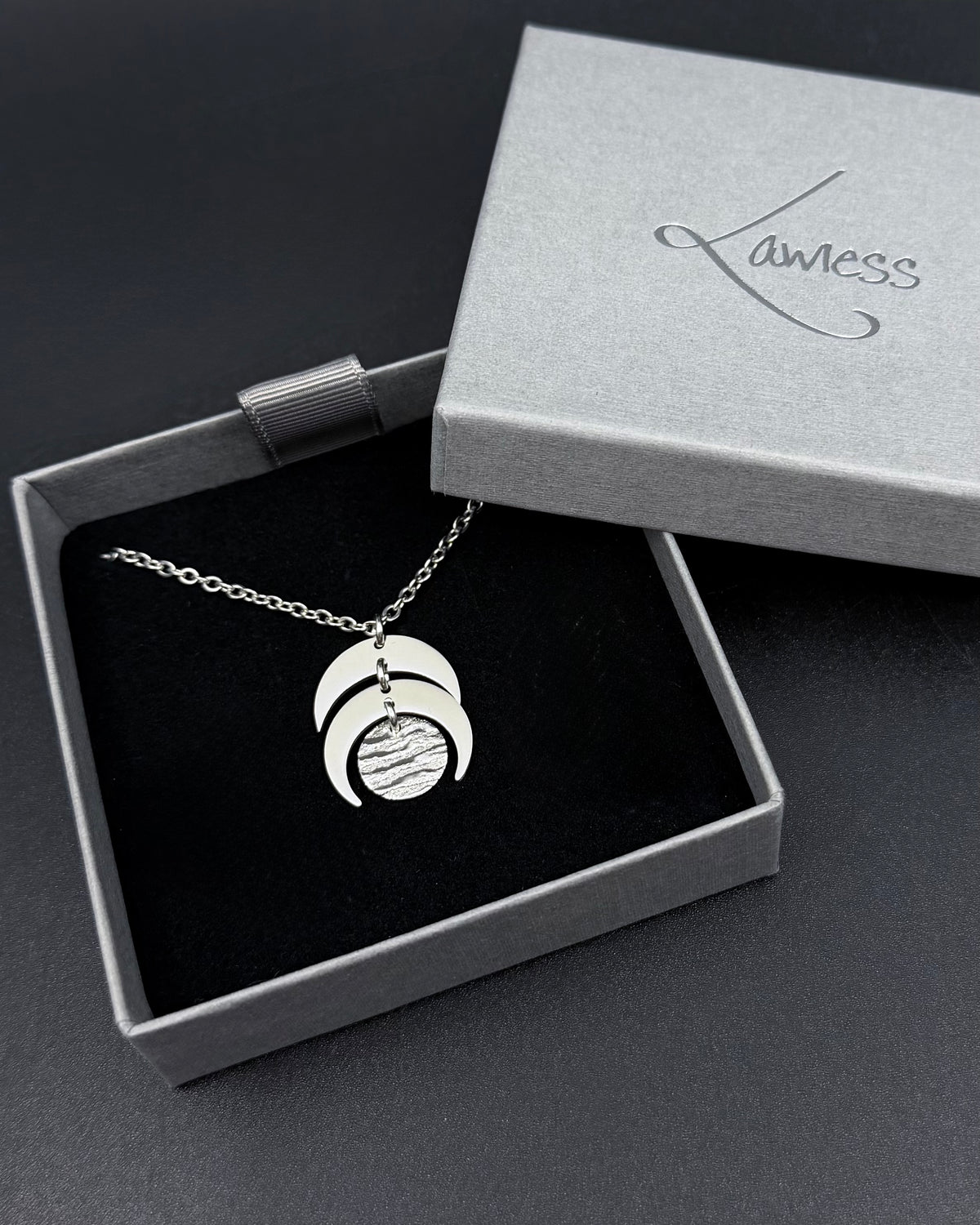 Silver Luna Phase necklace with sculptural crescent moon pendant and textured lunar disc on stainless steel chain, minimalist celestial design