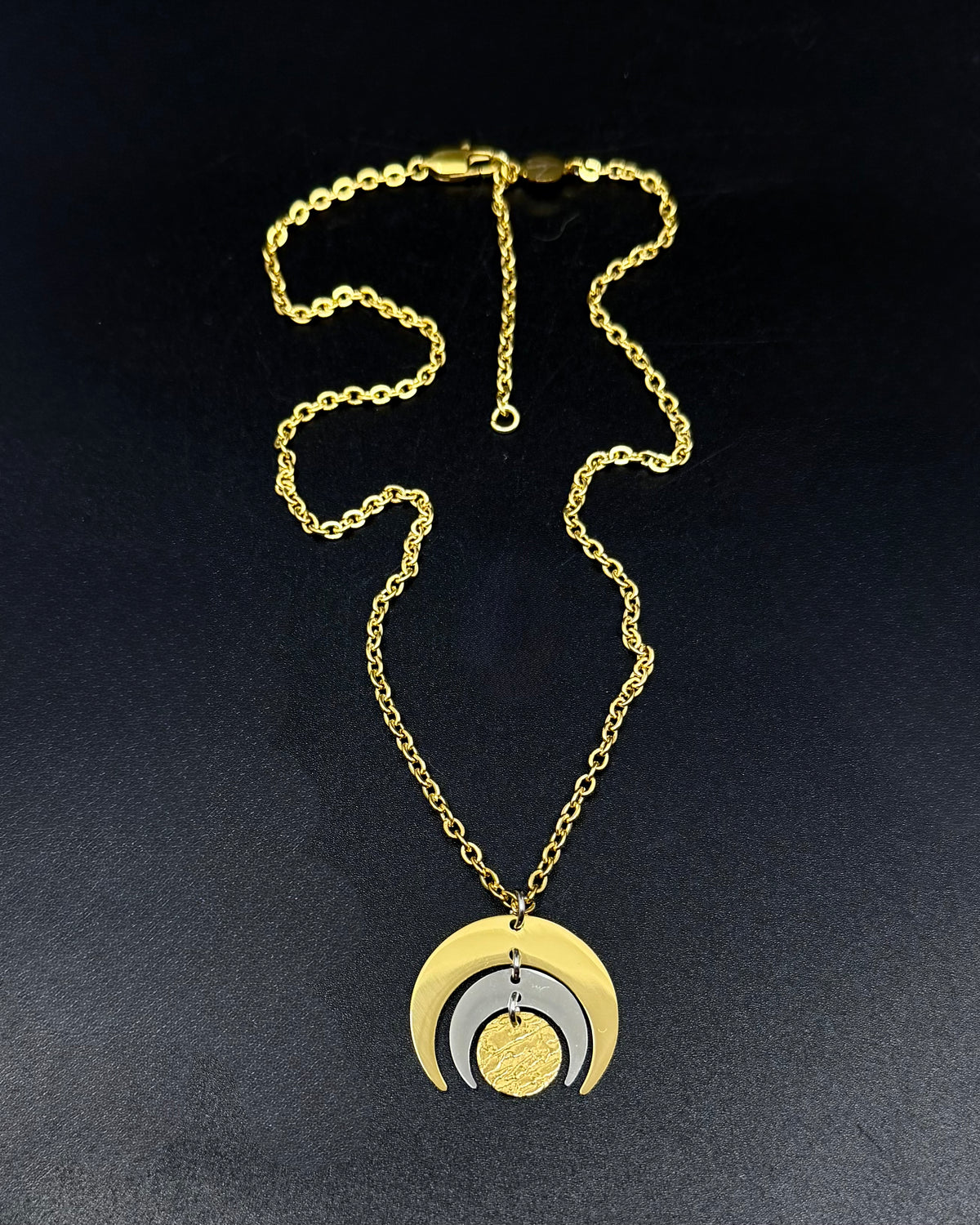 Gold and silver Luna Phase necklace with layered crescent moon pendant on a fine gold chain, photographed on a dark background.