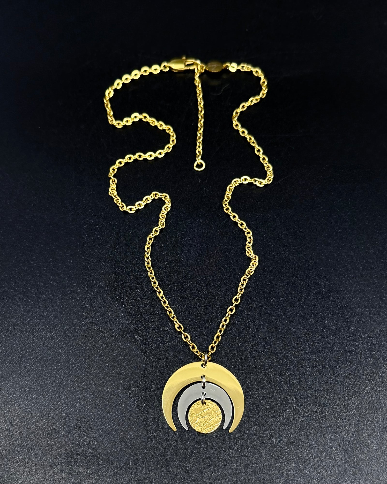 Gold and silver Luna Phase necklace with layered crescent moon pendant on a fine gold chain, photographed on a dark background.