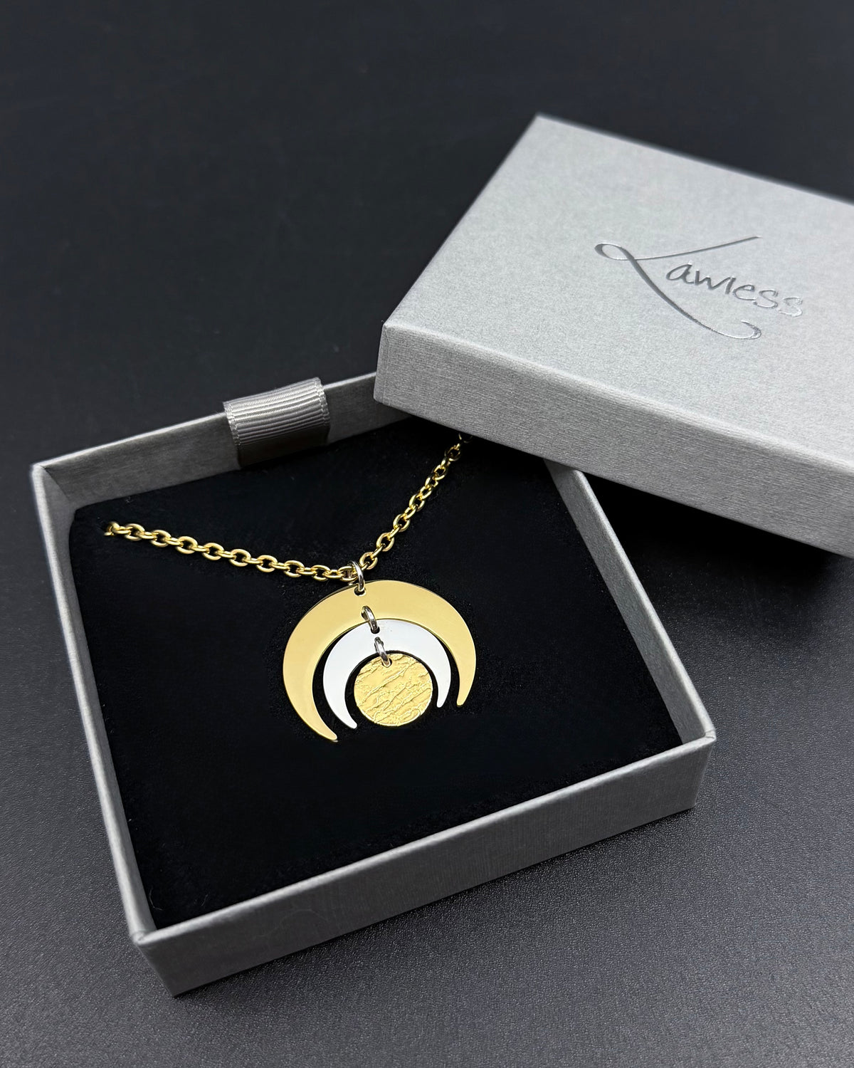 Gold and silver Luna Phase necklace with layered crescent moon pendant on a fine gold chain, photographed on a dark background.