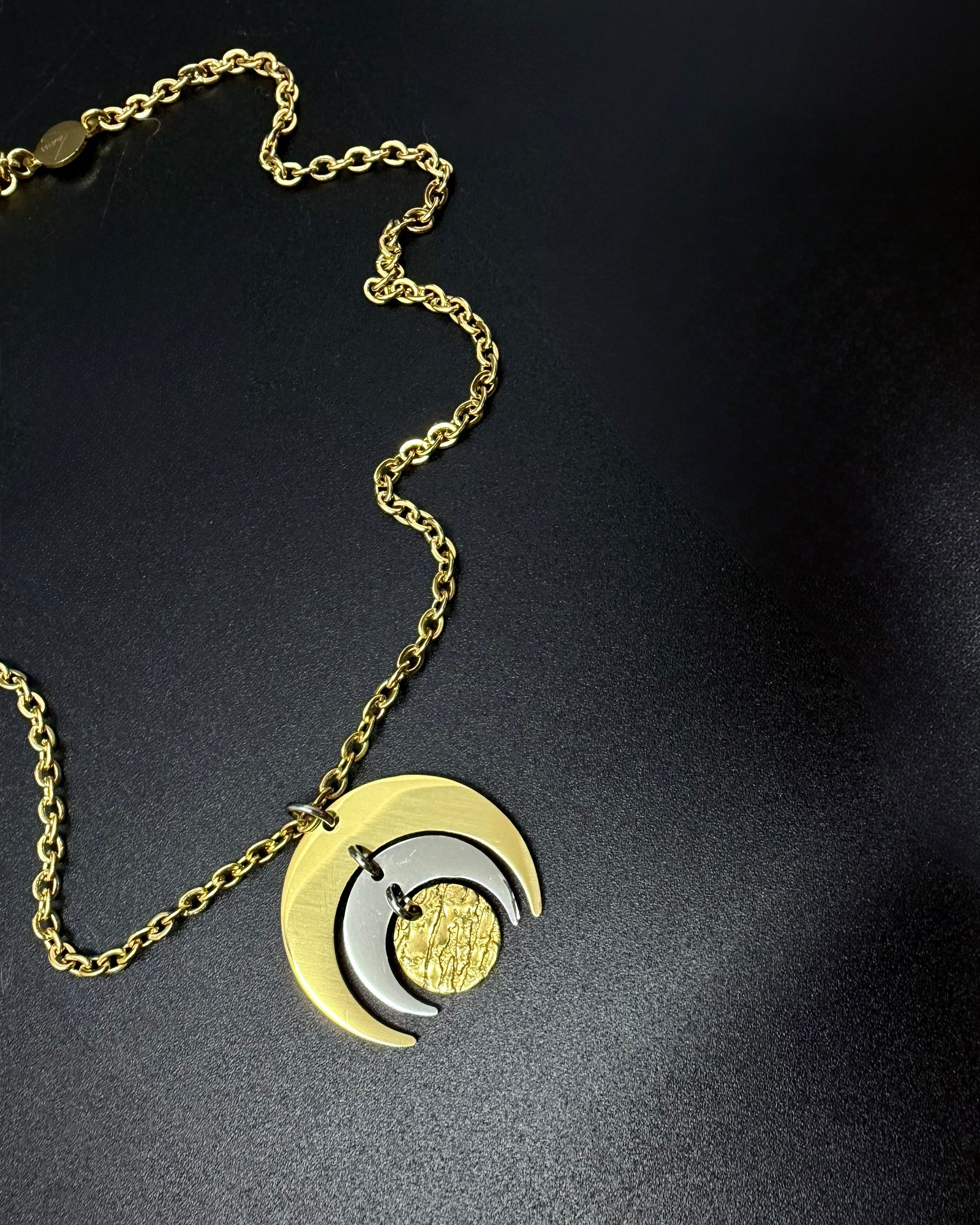 Gold and silver Luna Phase necklace with layered crescent moon pendant on a fine gold chain, photographed on a dark background.
