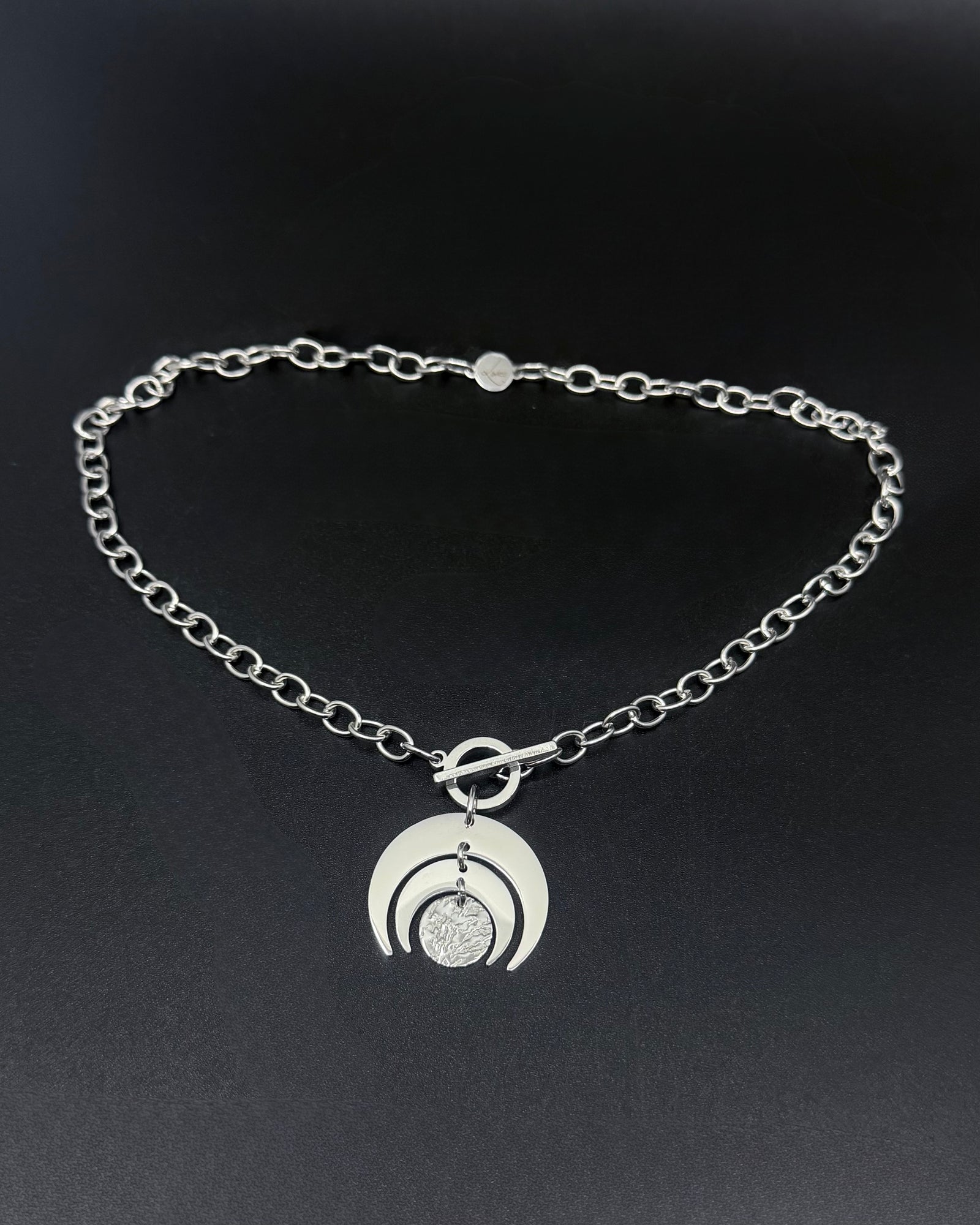Silver Luna Phase necklace with crescent moon pendant and textured disc on a stainless steel curb chain with toggle clasp.