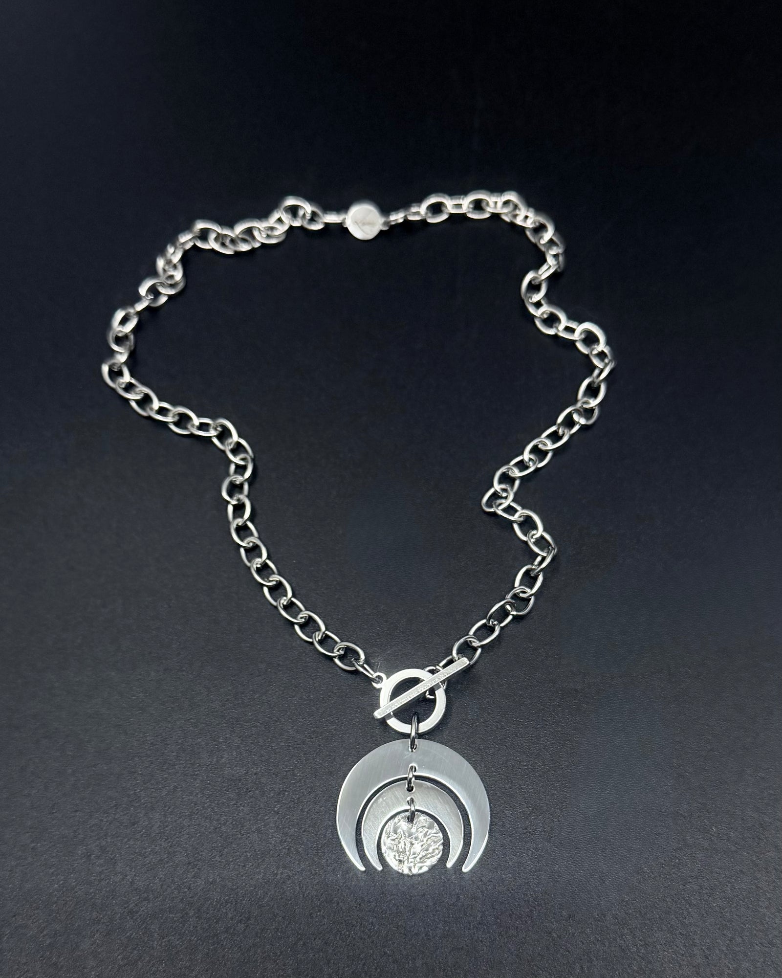 Silver Luna Phase necklace with crescent moon pendant and textured disc on a stainless steel curb chain with toggle clasp.