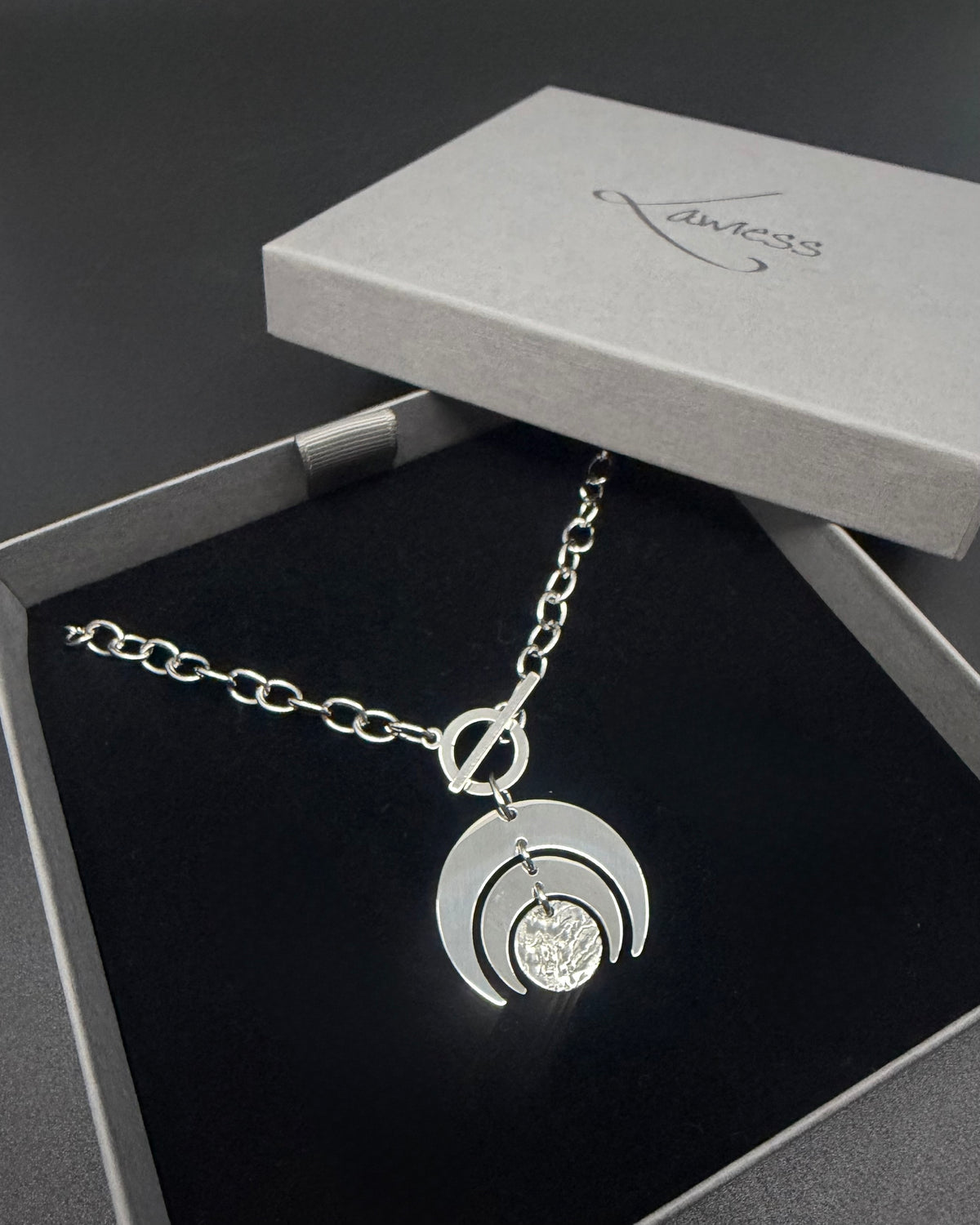 Silver Luna Phase necklace with crescent moon pendant and textured disc on a stainless steel curb chain with toggle clasp.