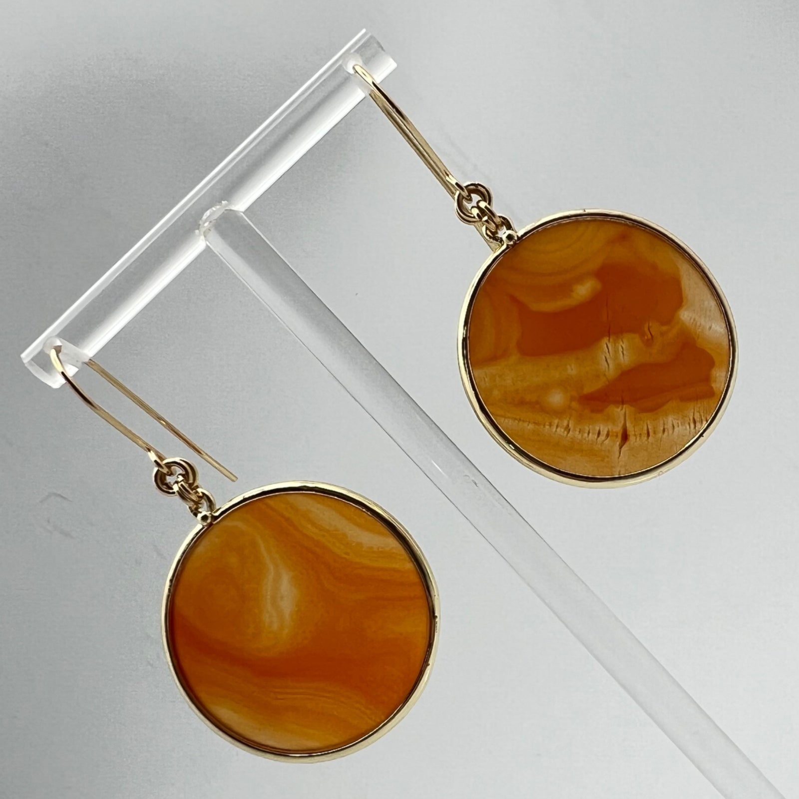 Gold-plated stainless steel earrings with 30 mm polished carnelian gemstone discs showing natural volcanic banding, 5 cm drop — Lawless Jewellery.