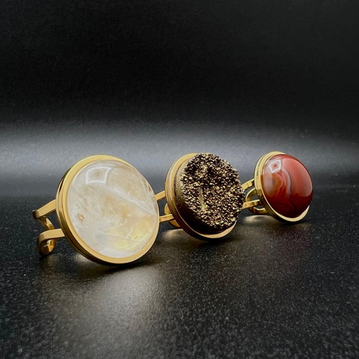Set of three gold-plated stainless steel rings featuring 20 mm cabochons in Clear Quartz, Gold Druzy, and Carnelian on adjustable double-shank bands — Lawless Jewellery.