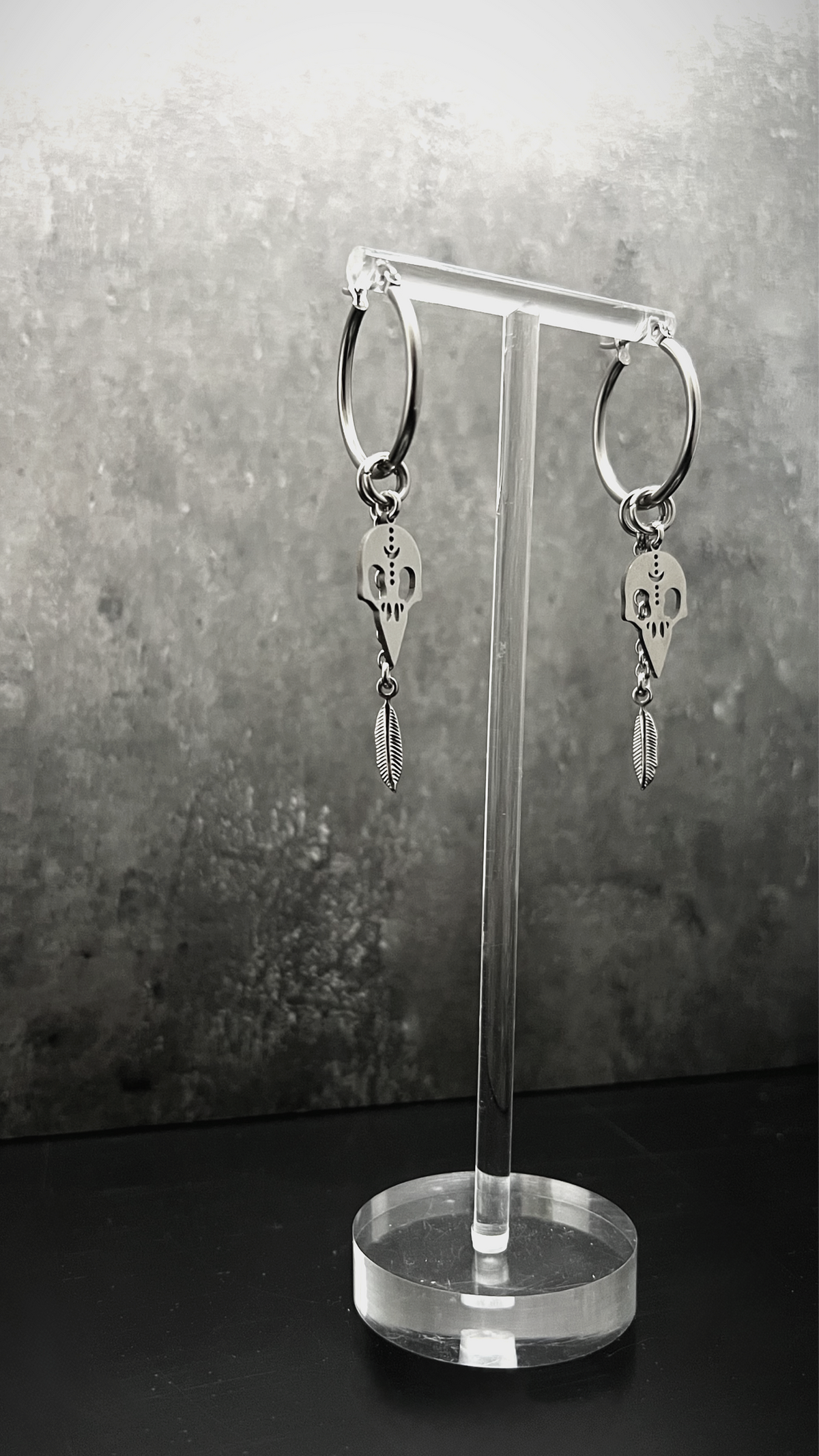 All-silver stainless steel hoop earrings featuring skull and feather charms, sculptural lightweight design — Lawless Jewellery.