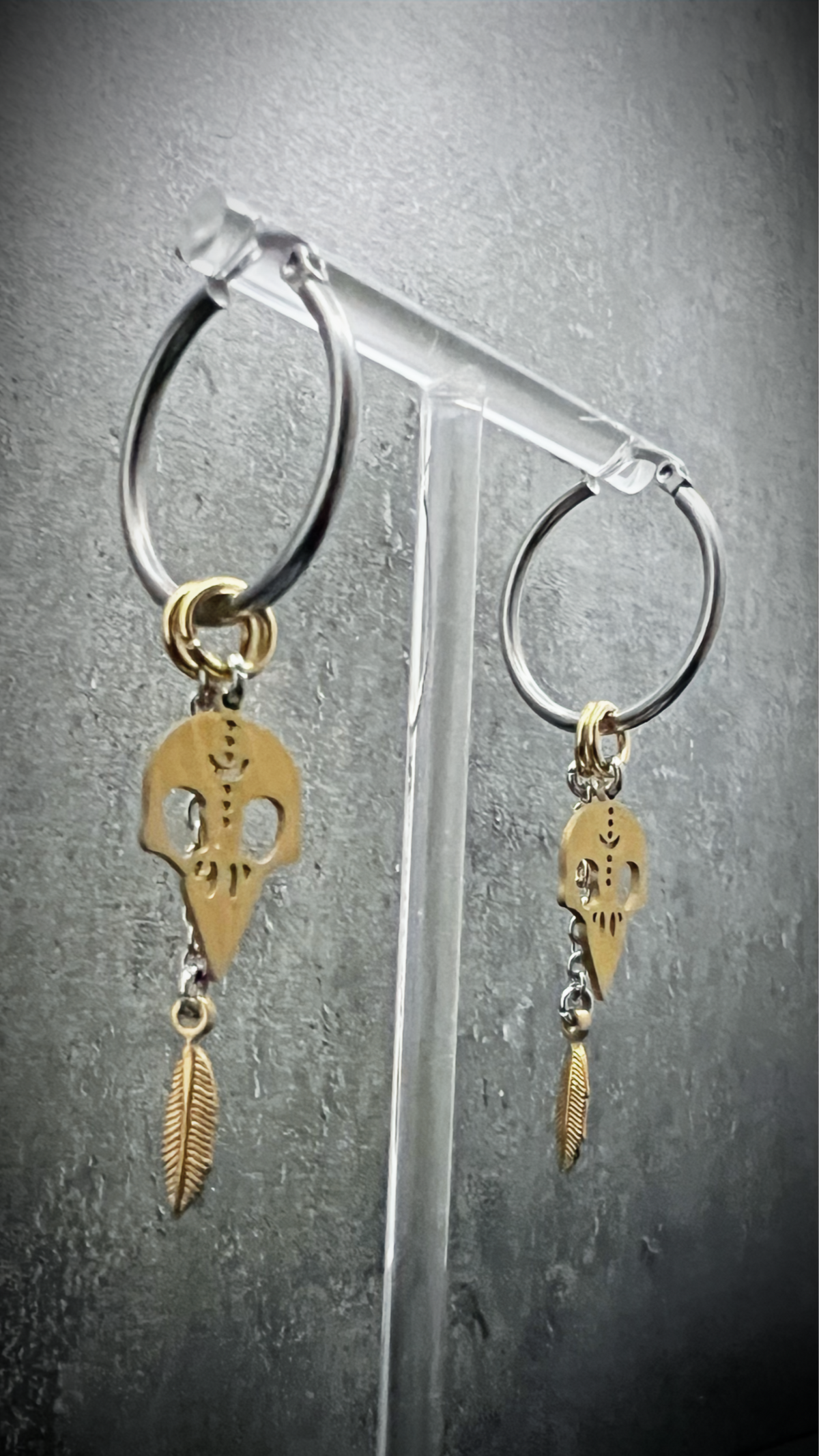 Silver stainless steel hoop earrings featuring gold skull and feather charms, lightweight dual-tone design — Lawless Jewellery.