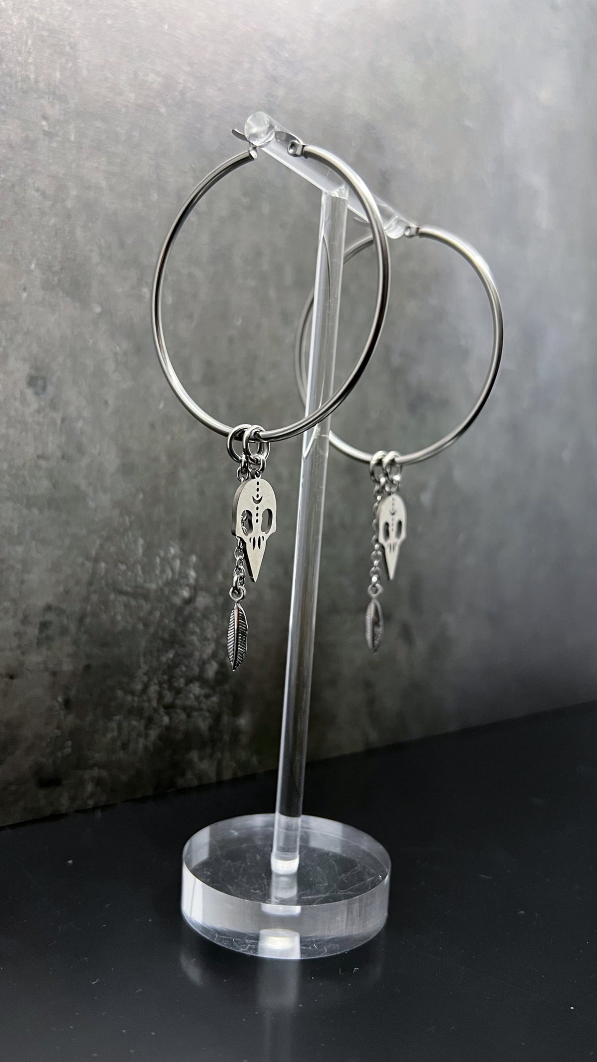 Oversized all-silver stainless steel hoop earrings featuring sculptural skull and feather charms — bold yet lightweight design — Lawless Jewellery.