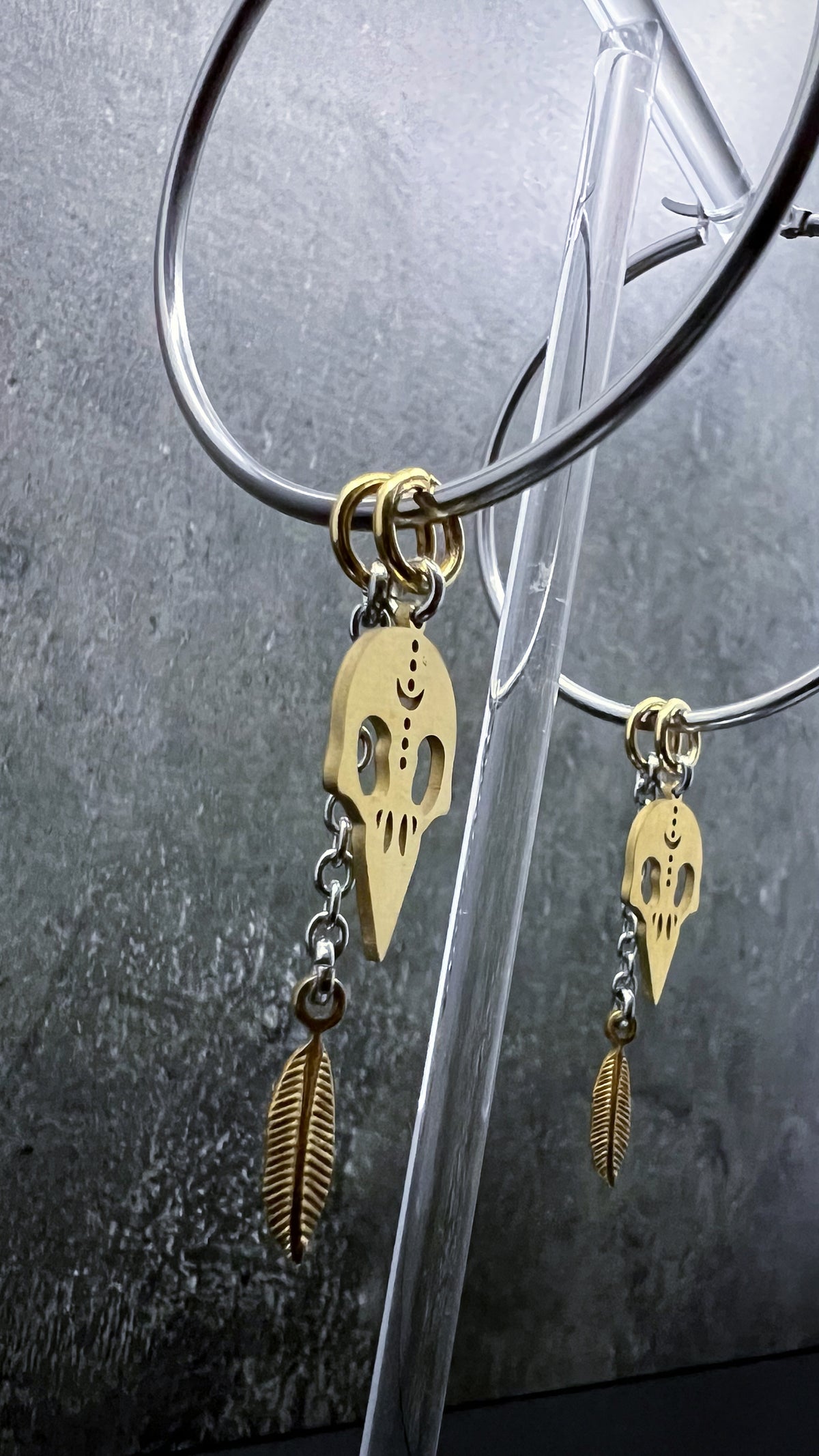 Oversized all-silver stainless steel hoop earrings featuring sculptural skull and feather charms — bold yet lightweight design — Lawless Jewellery.