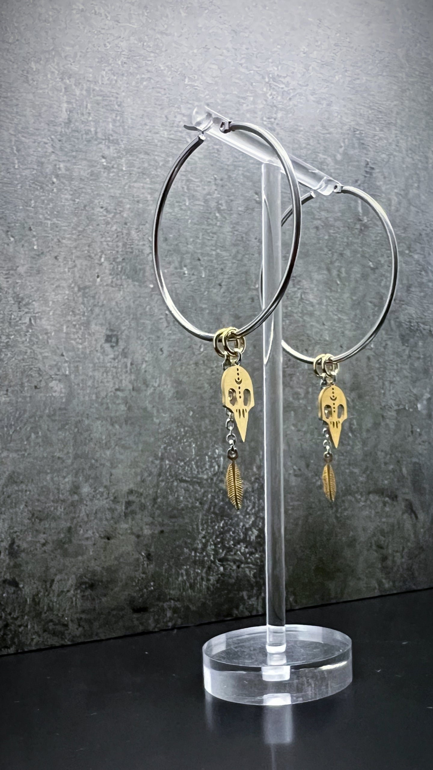 Oversized all-silver stainless steel hoop earrings featuring sculptural skull and feather charms — bold yet lightweight design — Lawless Jewellery.