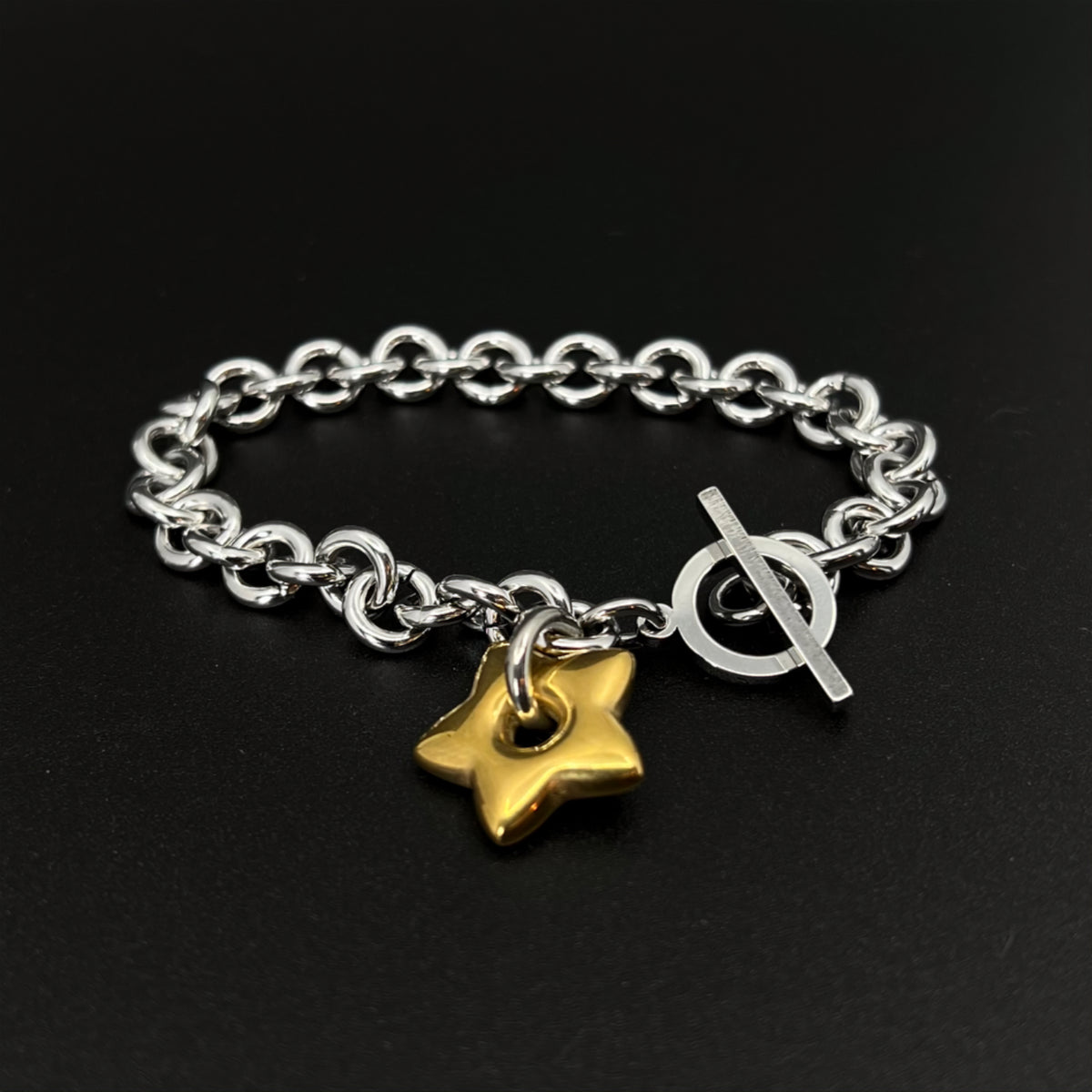 Mixed-metal stainless steel Unisex bracelet featuring an 18mm gold star charm on a silver chain with toggle clasp, photographed on a dark background.