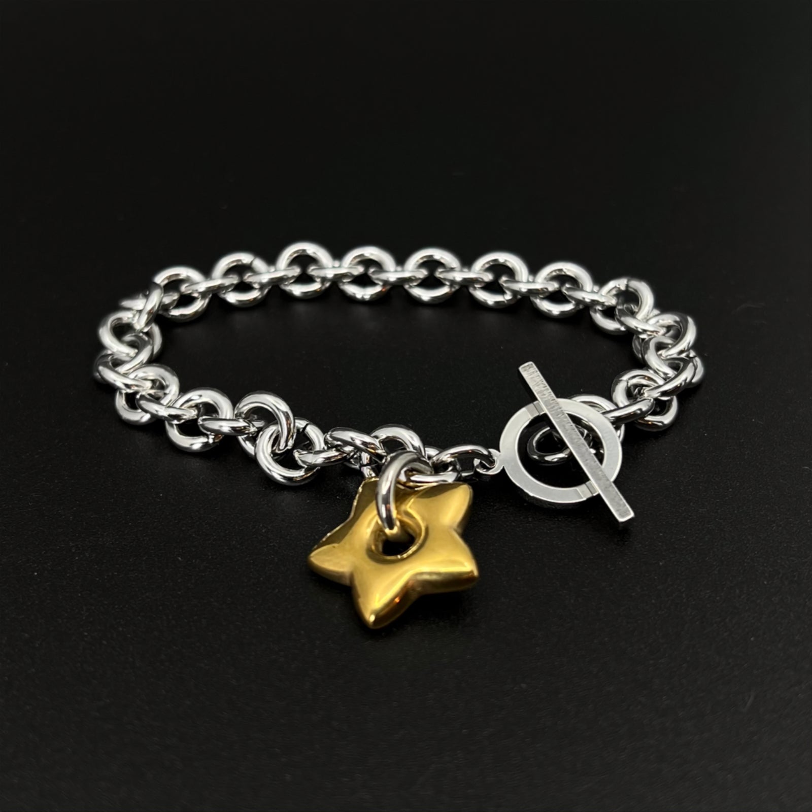 Mixed-metal stainless steel Unisex bracelet featuring an 18mm gold star charm on a silver chain with toggle clasp, photographed on a dark background.