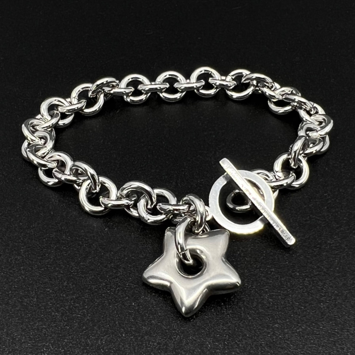 All-silver stainless steel bracelet featuring an 18mm star charm on a polished chain with toggle clasp, photographed on a dark background.