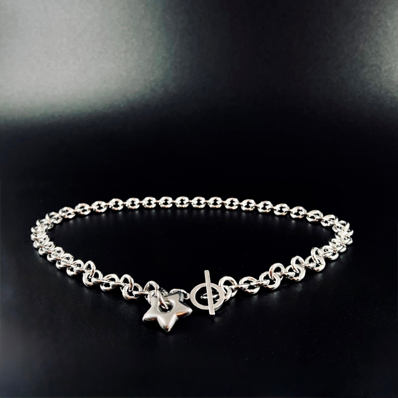 Silver stainless steel chain necklace with gold star pendant and toggle clasp, Urania Axis Necklace by Lawless Jewellery on black background