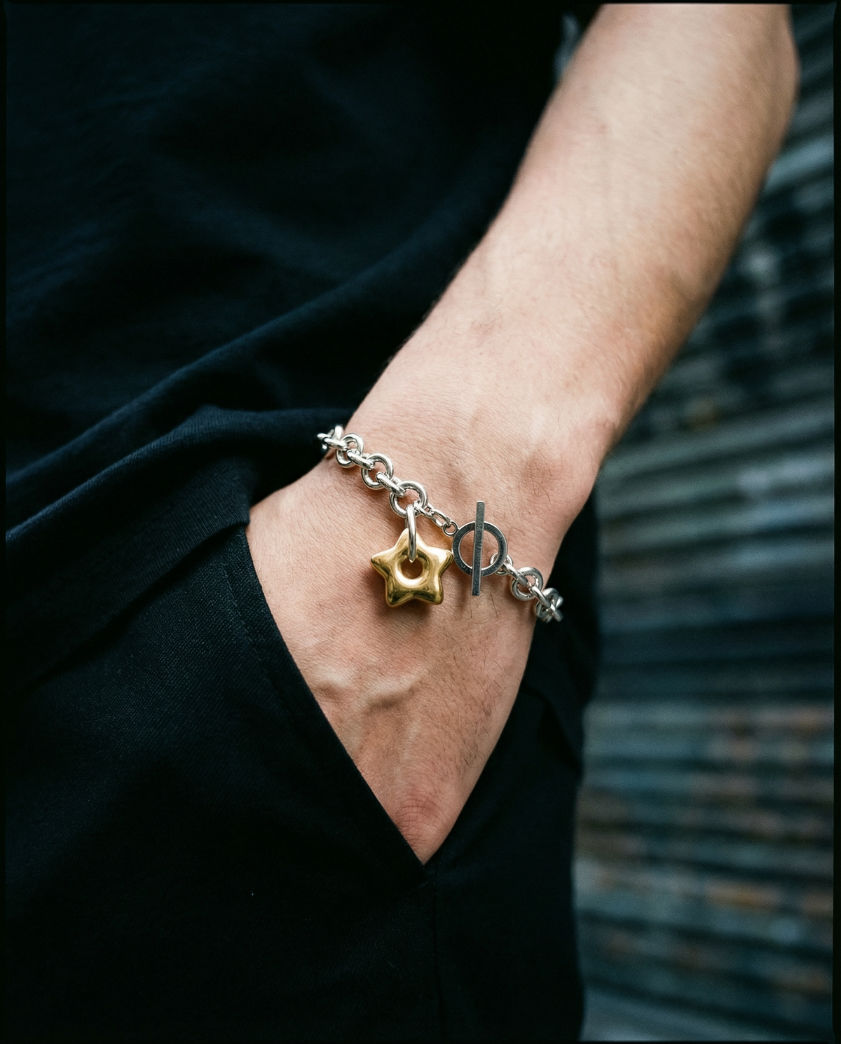 Mixed-metal stainless steel Unisex bracelet featuring an 18mm gold star charm on a silver chain with toggle clasp, photographed on a dark background.
