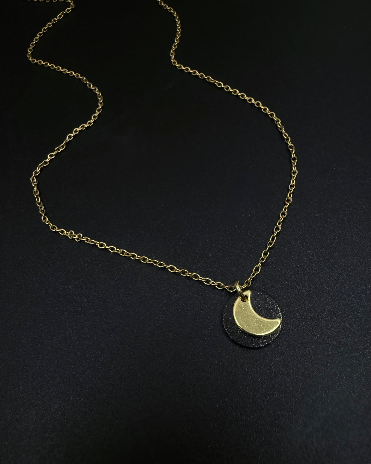 Black and gold Urania Signal necklace with matte black disc and gold crescent moon pendant on adjustable stainless steel chain.
