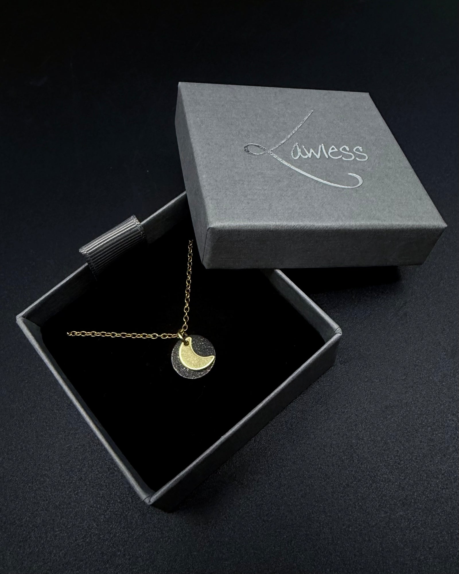 Black and gold Urania Signal necklace with matte black disc and gold crescent moon pendant on adjustable stainless steel chain.