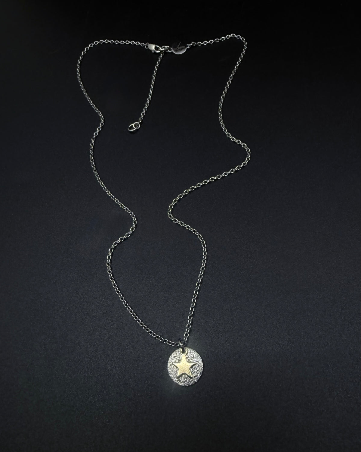 Silver and gold Urania Signal Star Necklace featuring a textured silver disc with a polished gold star charm on an adjustable stainless steel chain