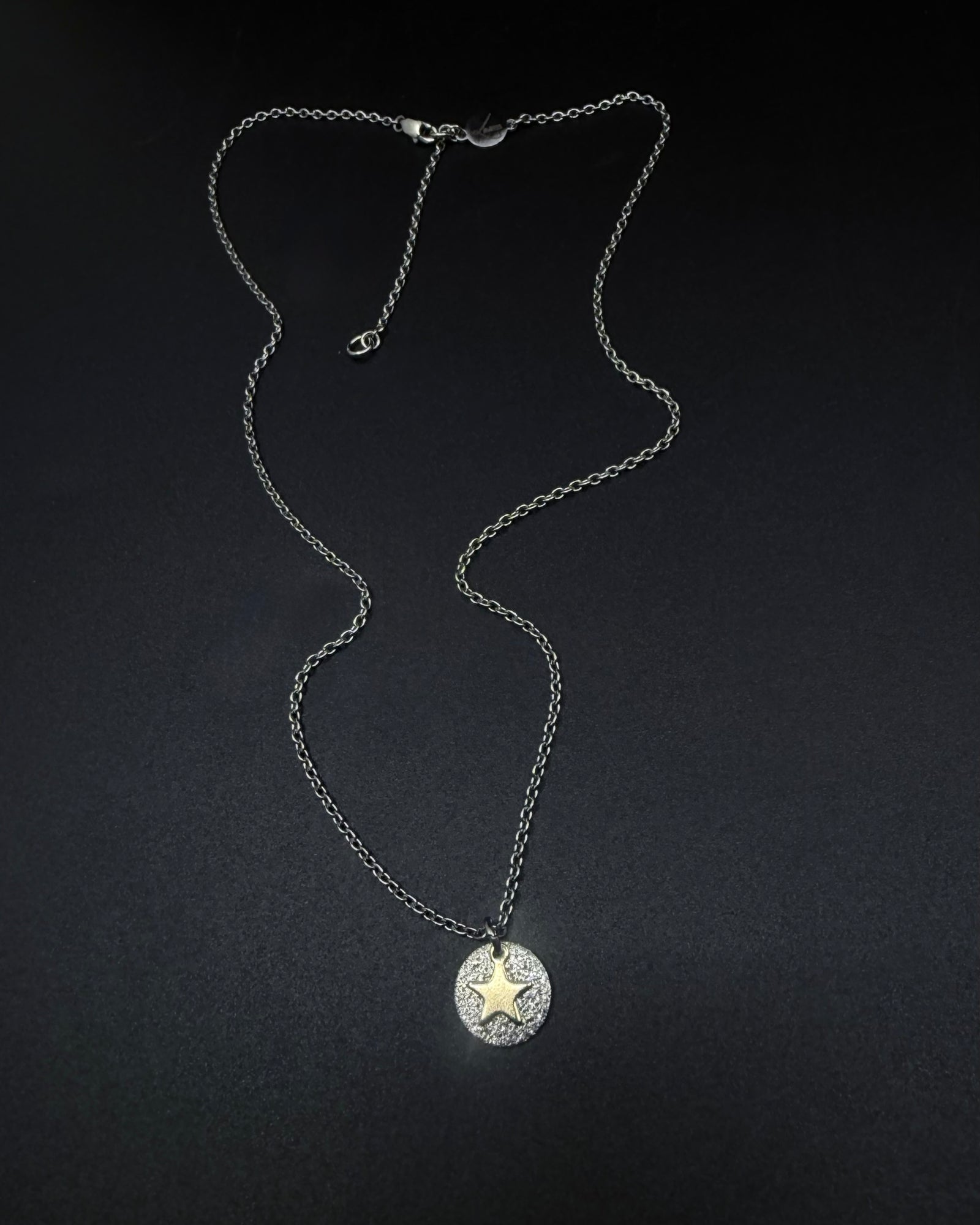 Silver and gold Urania Signal Star Necklace featuring a textured silver disc with a polished gold star charm on an adjustable stainless steel chain