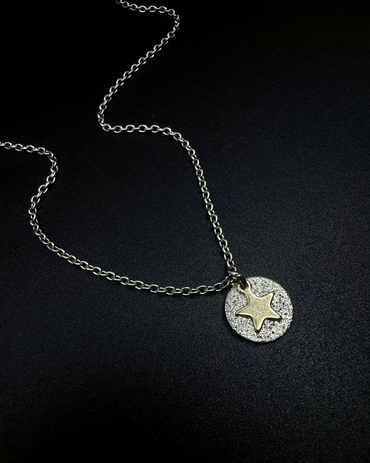 Silver and gold Urania Signal Star Necklace featuring a textured silver disc with a polished gold star charm on an adjustable stainless steel chain